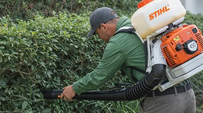 Pest control technician applying mosquito treatment directly into dense shrubs at a Florida home