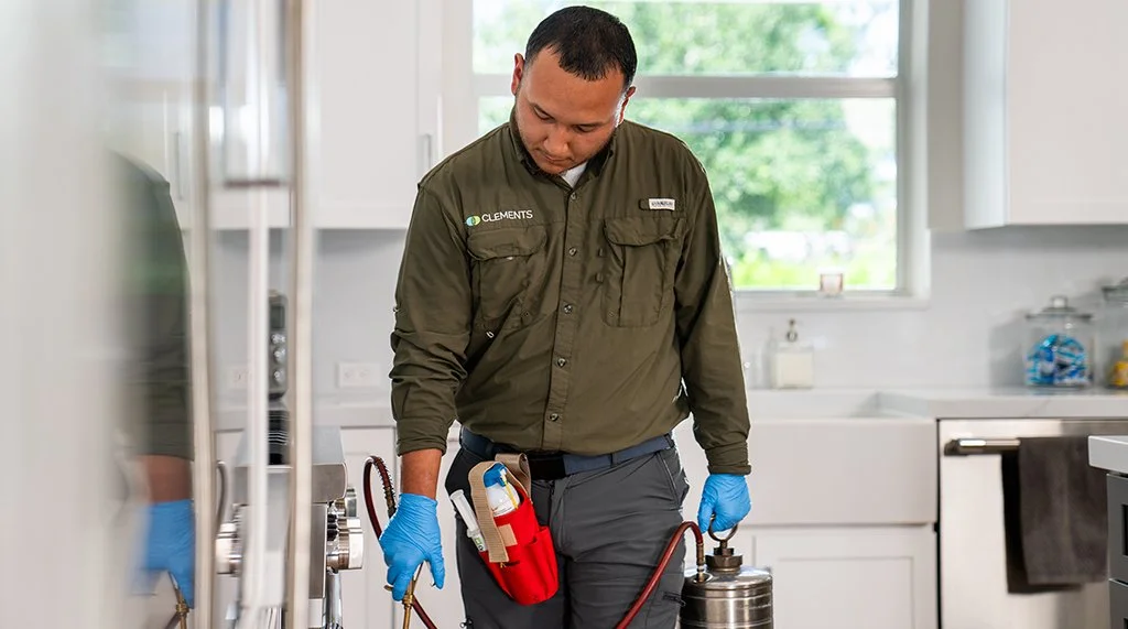 A Clements Pest Control technician applying pesticide in a kitchen