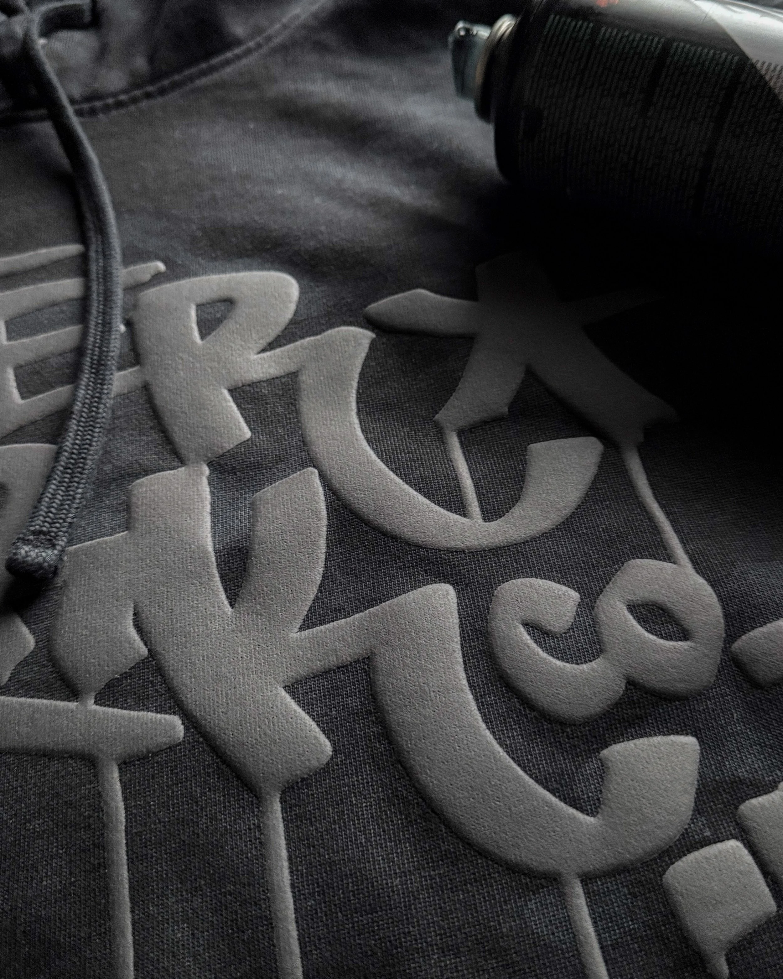Close-up of raised Black Puff lettering on a District Wash Camo Fleece Hoodie.