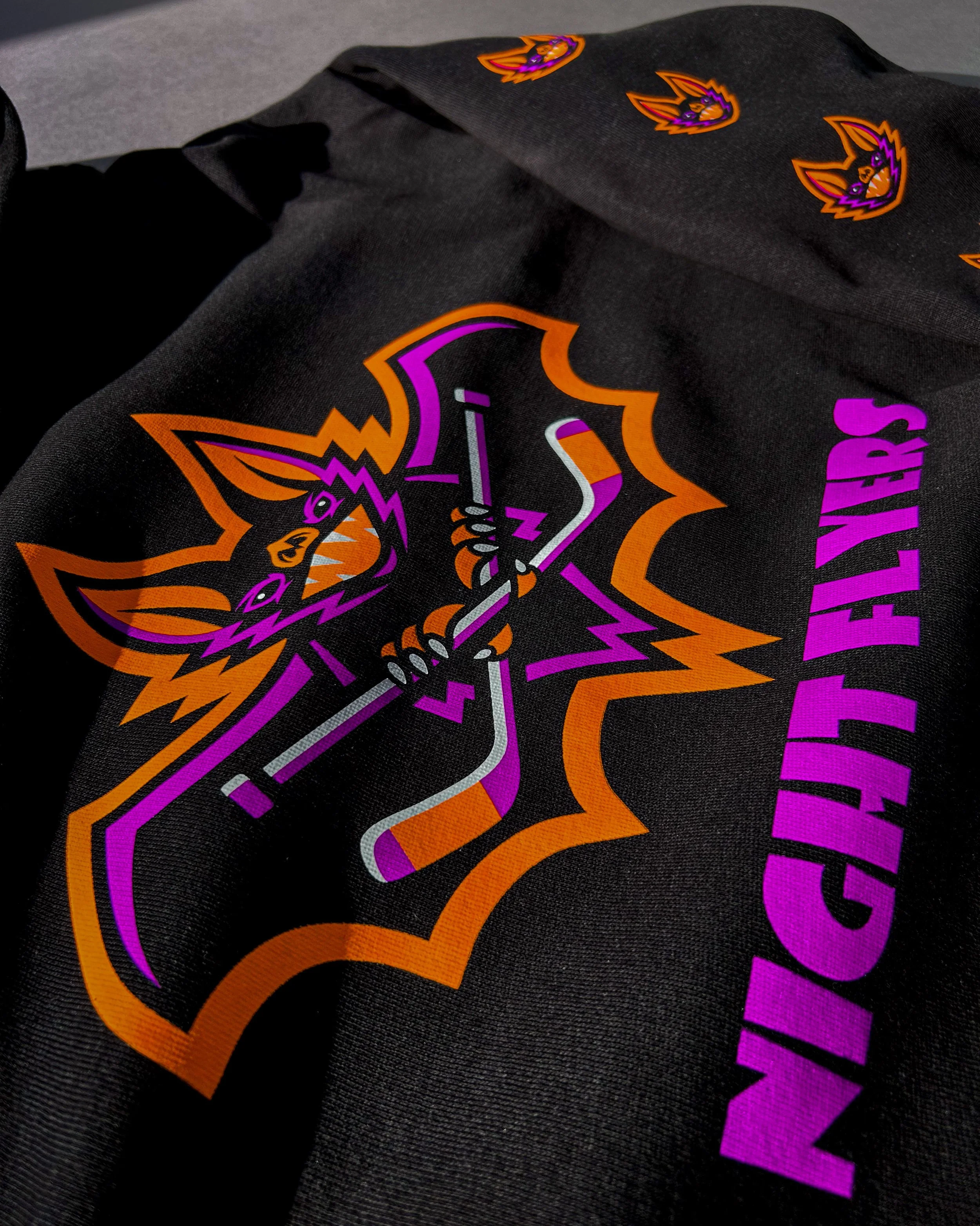 Close-up of a Night Flyers hockey graphic in Neon Orange, Neon Purple and White Howard Multi-Purpose on a black hoodie.