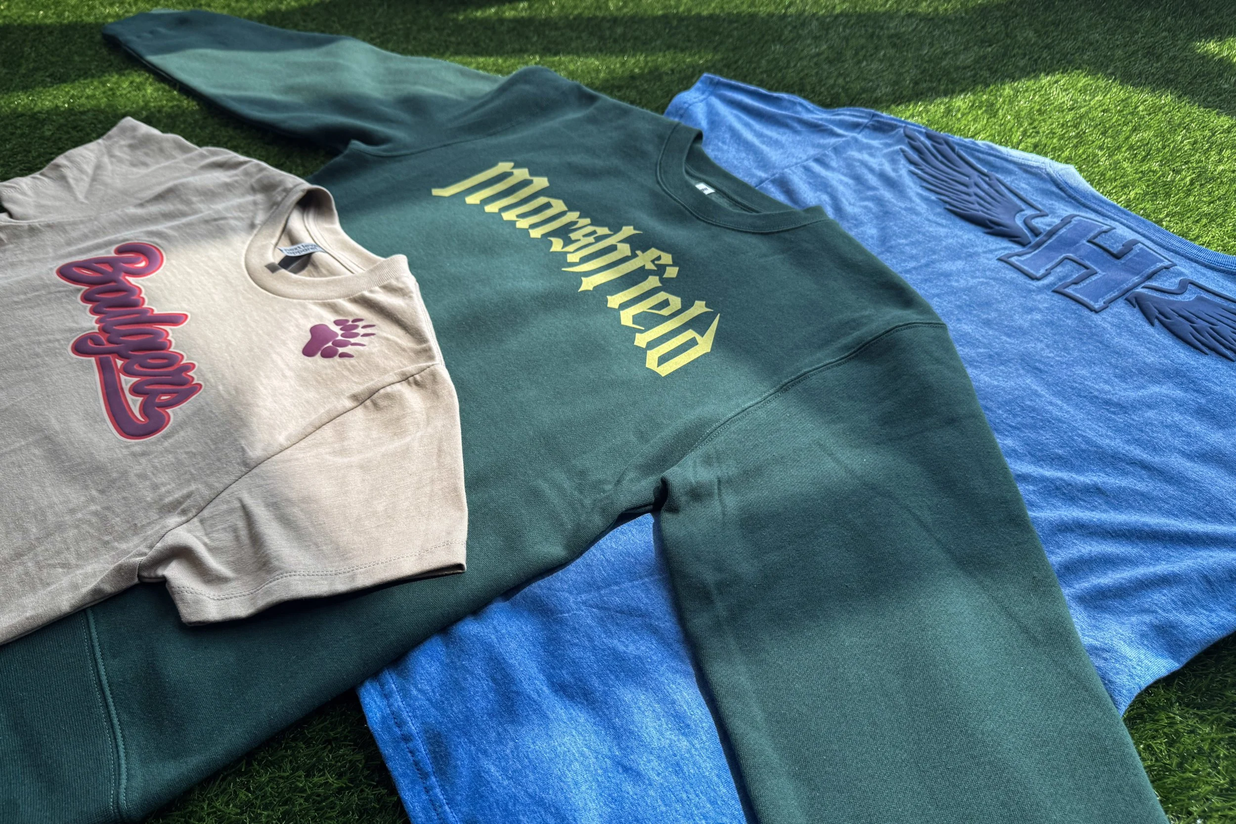 Three-piece Student Lifestyle school spirit wear collection featuring a ring-spun cotton tee with Puff, a fleece crewneck with Vintage Wash, and a heather tee with Shimmer and Puff screen printed heat transfers