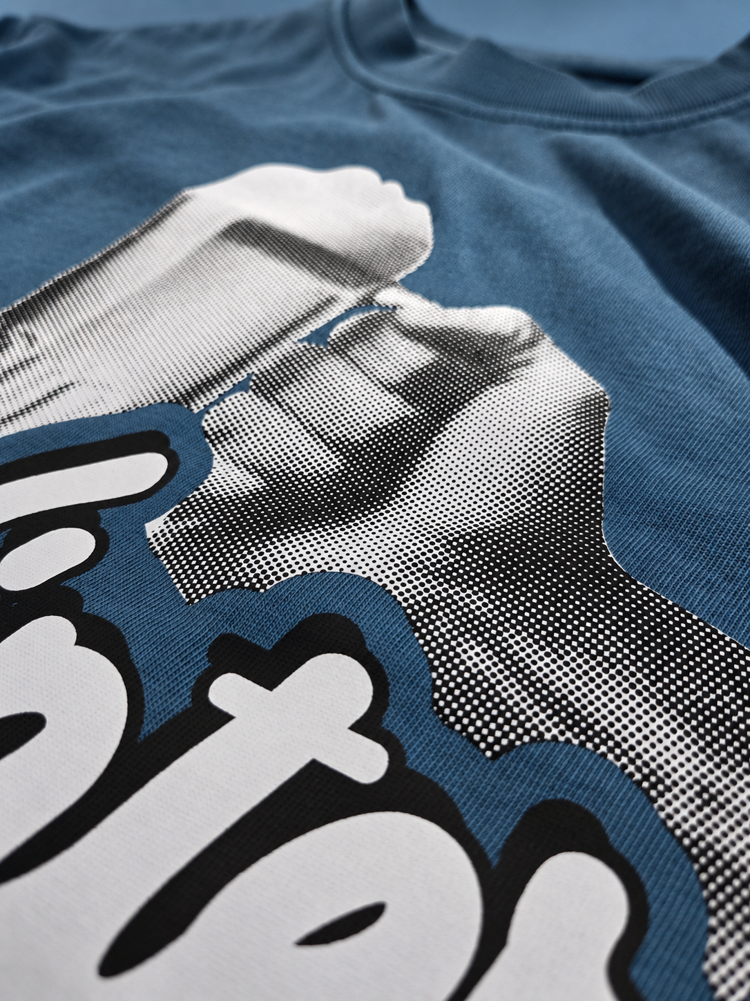 Close-up of black and white halftone beer artwork on garment-dyed blue cotton