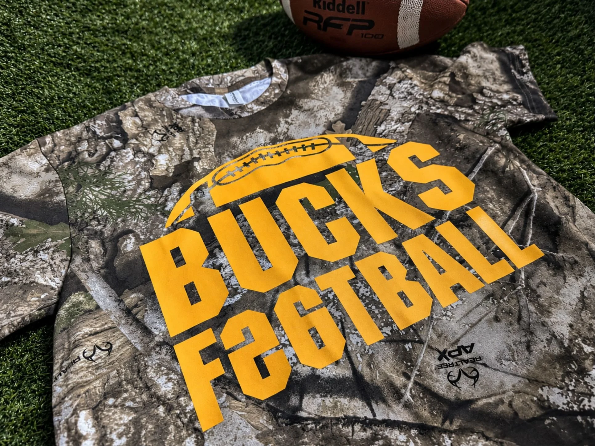 Bucks Football Realtree APX camo tee with Athletic Gold Howard Multi-Purpose designed as recognizable team spirit wear.