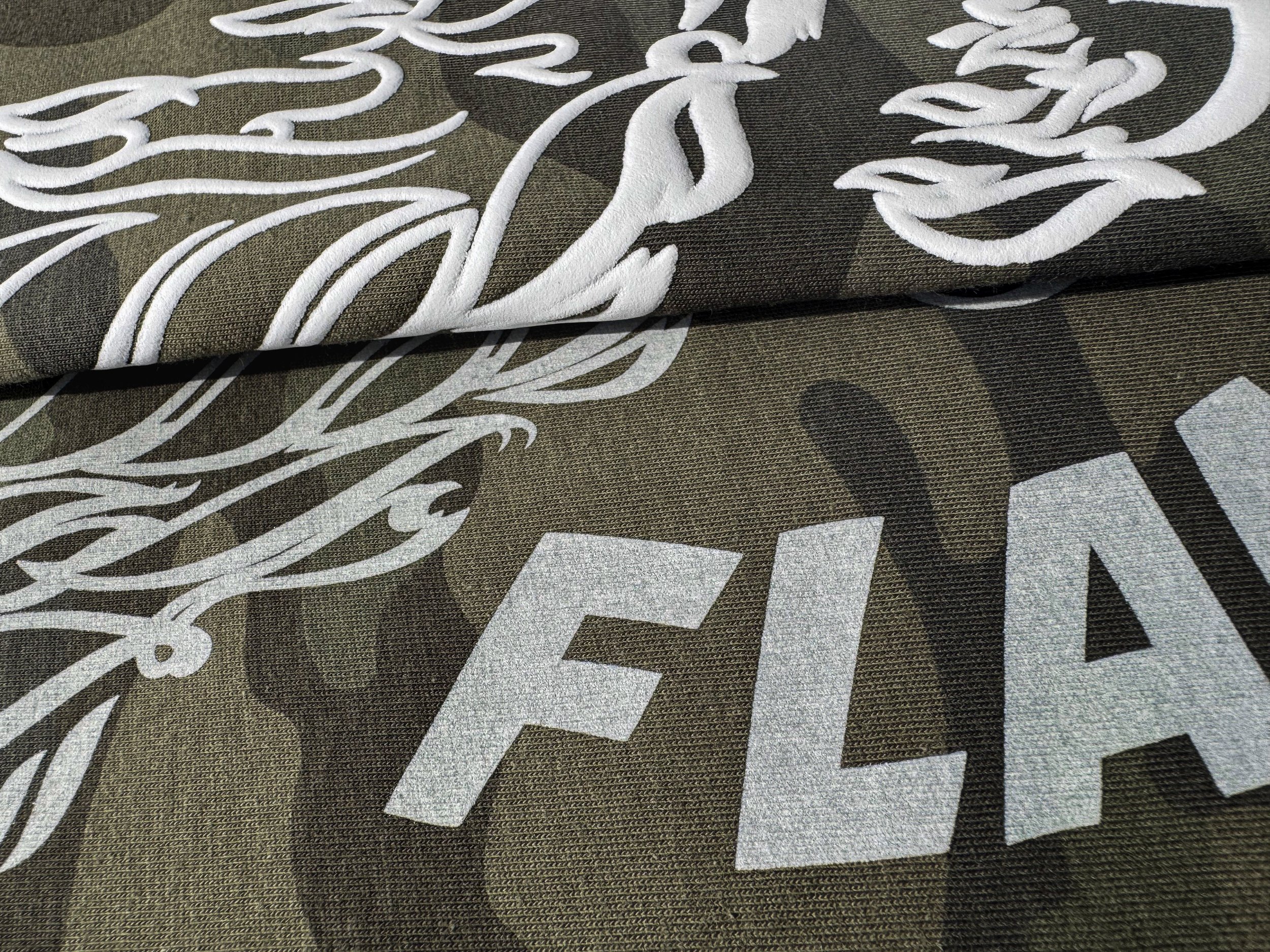 Close-up of the same Flame Throwers artwork printed in white Puff and Vintage Wash on Forest Camo tees.
