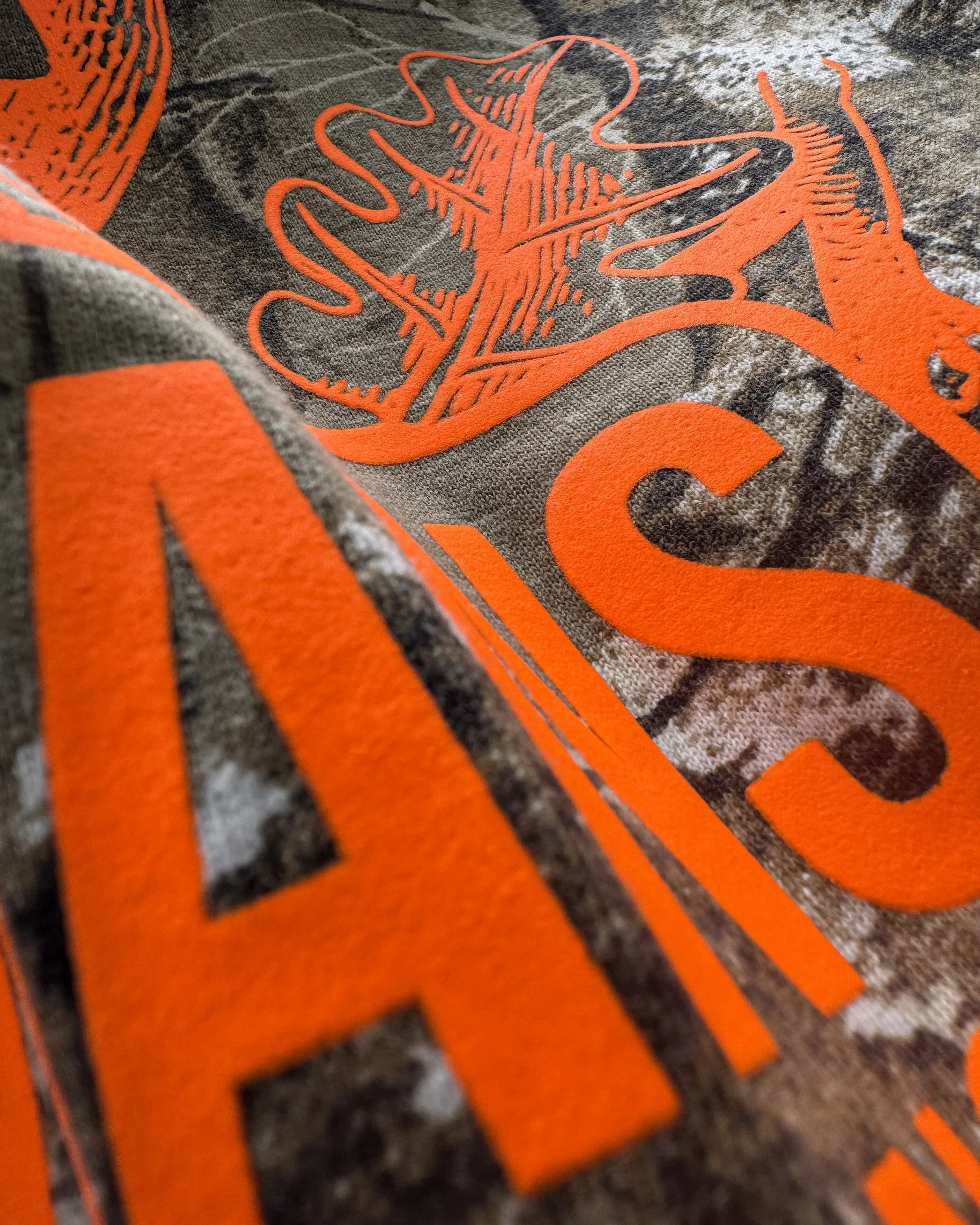 Close-up of detailed Neon Orange Howard Multi-Purpose lettering and outdoor artwork on Realtree camo.