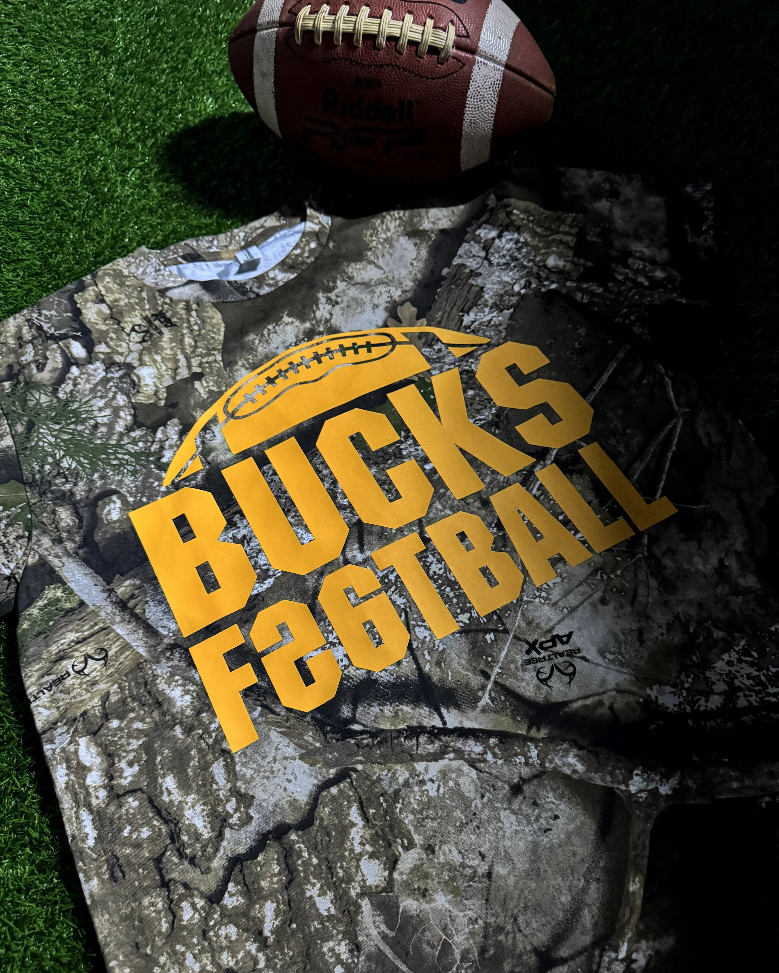 Bucks Football Realtree APX camo tee with an Athletic Gold Howard Multi-Purpose graphic.