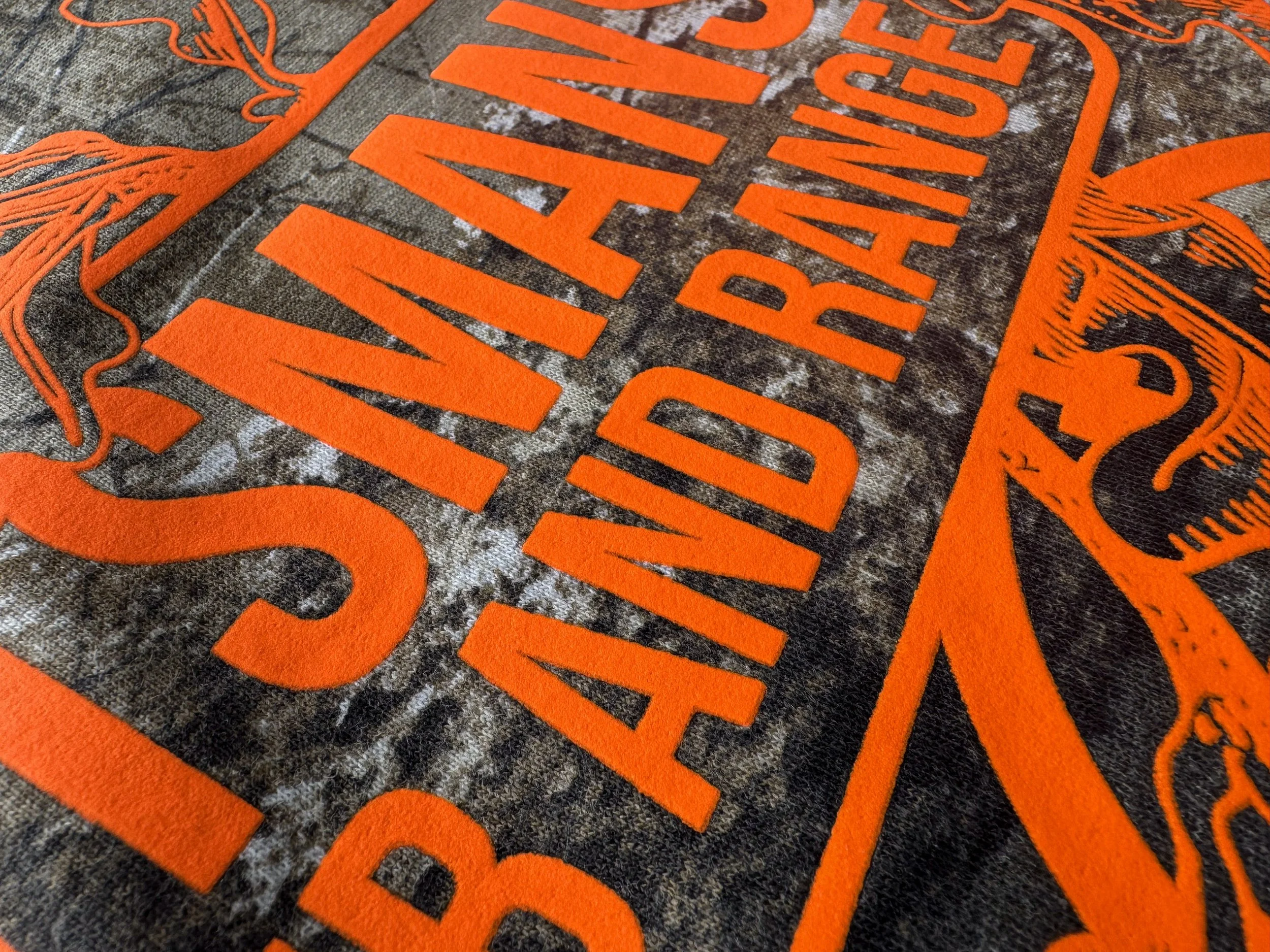 Close-up of Neon Orange Howard Multi-Purpose creating purposeful contrast over a detailed Realtree camo pattern.