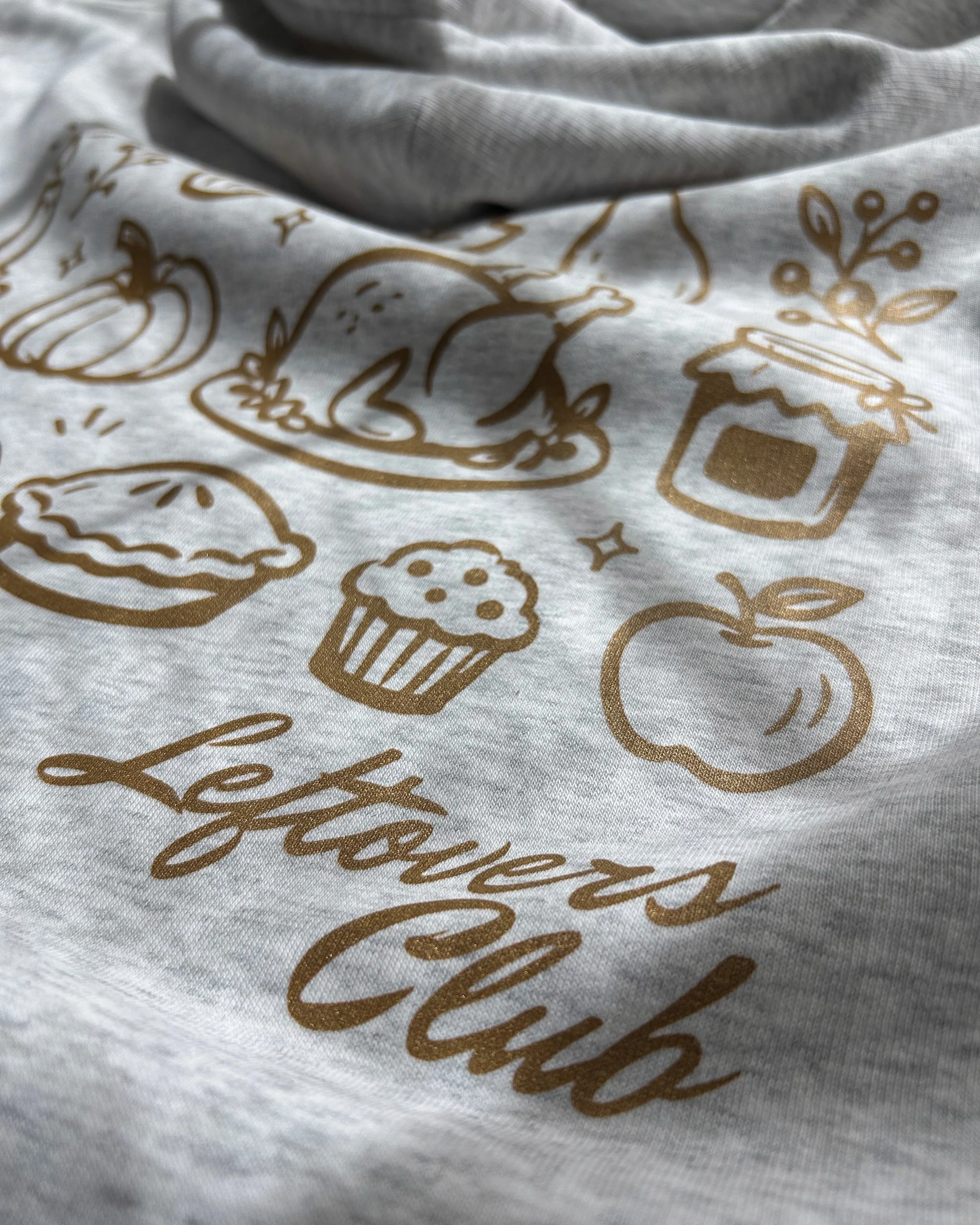Close-up of Leftovers Club food-and-gathering artwork printed with Howard Hot Peel in Copper Shimmer on an ash grey Stanley/Stella hoodie.