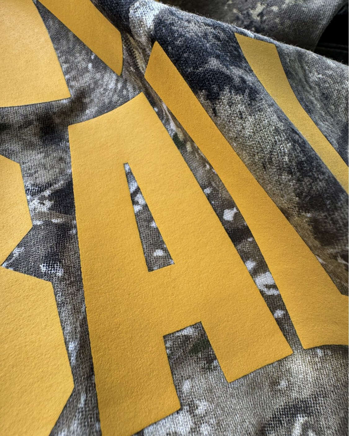 Close-up of opaque Athletic Gold Howard Multi-Purpose lettering printed over Realtree APX camo.