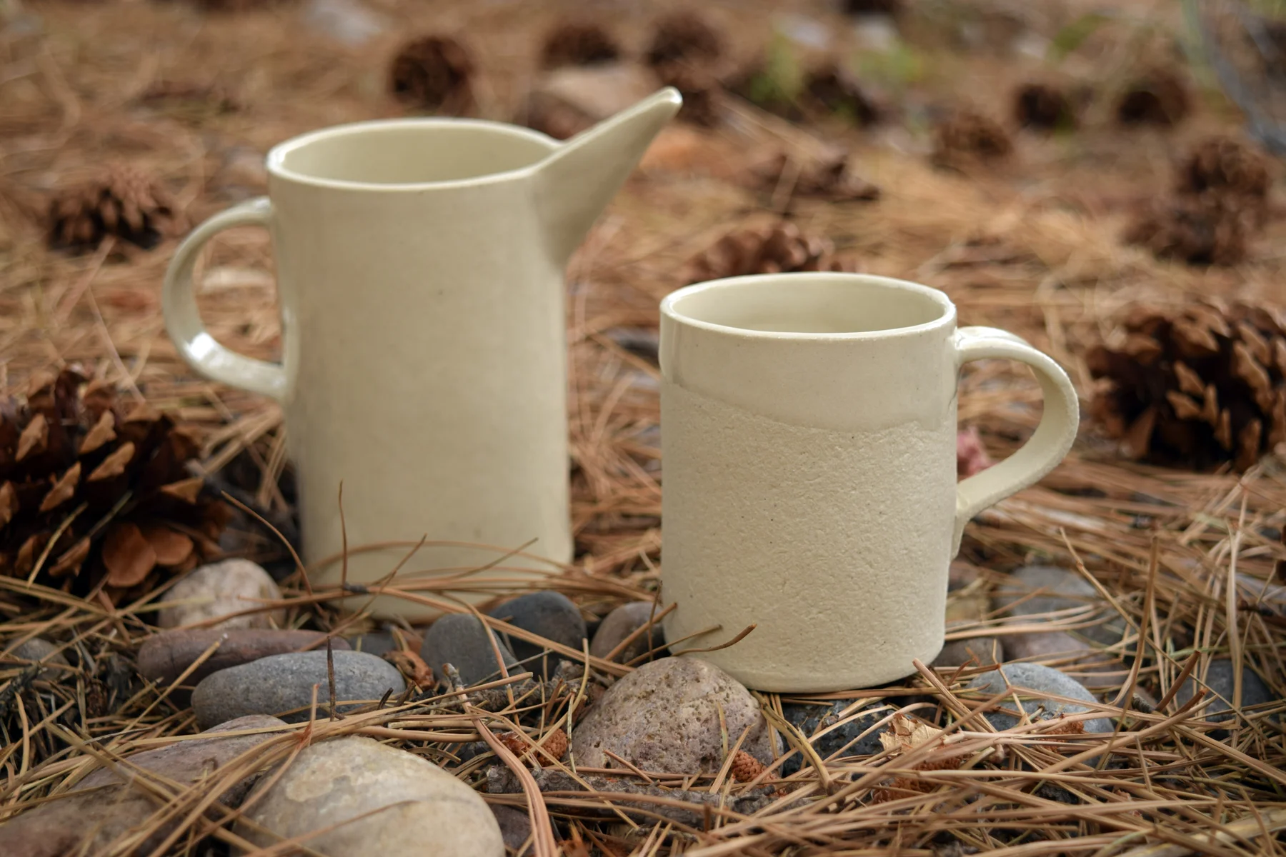 Limestone mug and creamer on pine needles and stones.