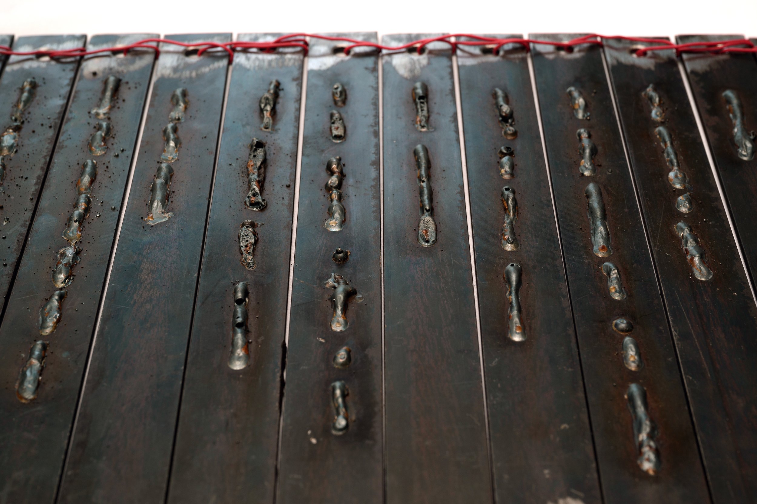   Scar Writings (detail)  2024  62 mild steel slip weldings, red wire, wood table 120cm by 40cm by 100cm 