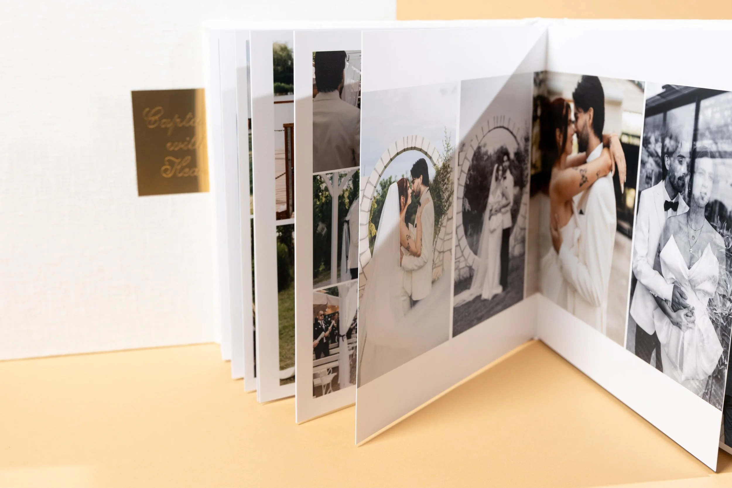 Photograph of a folded photo album displaying pictures of a wedding, including a couple embracing and posing outdoors, with a Gold label on the side that reads "Capture in Time".