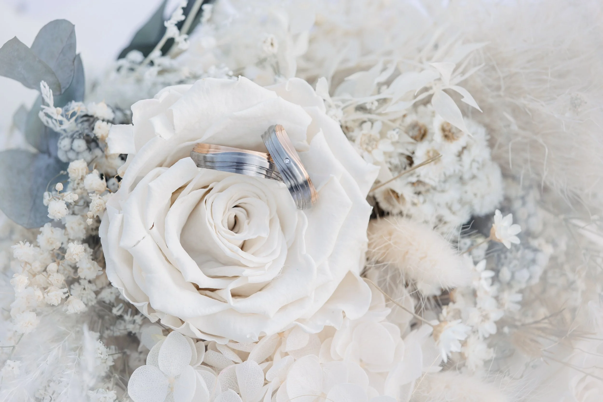 Close-up of a white floral arrangement with wedding rings resting on a white rose.