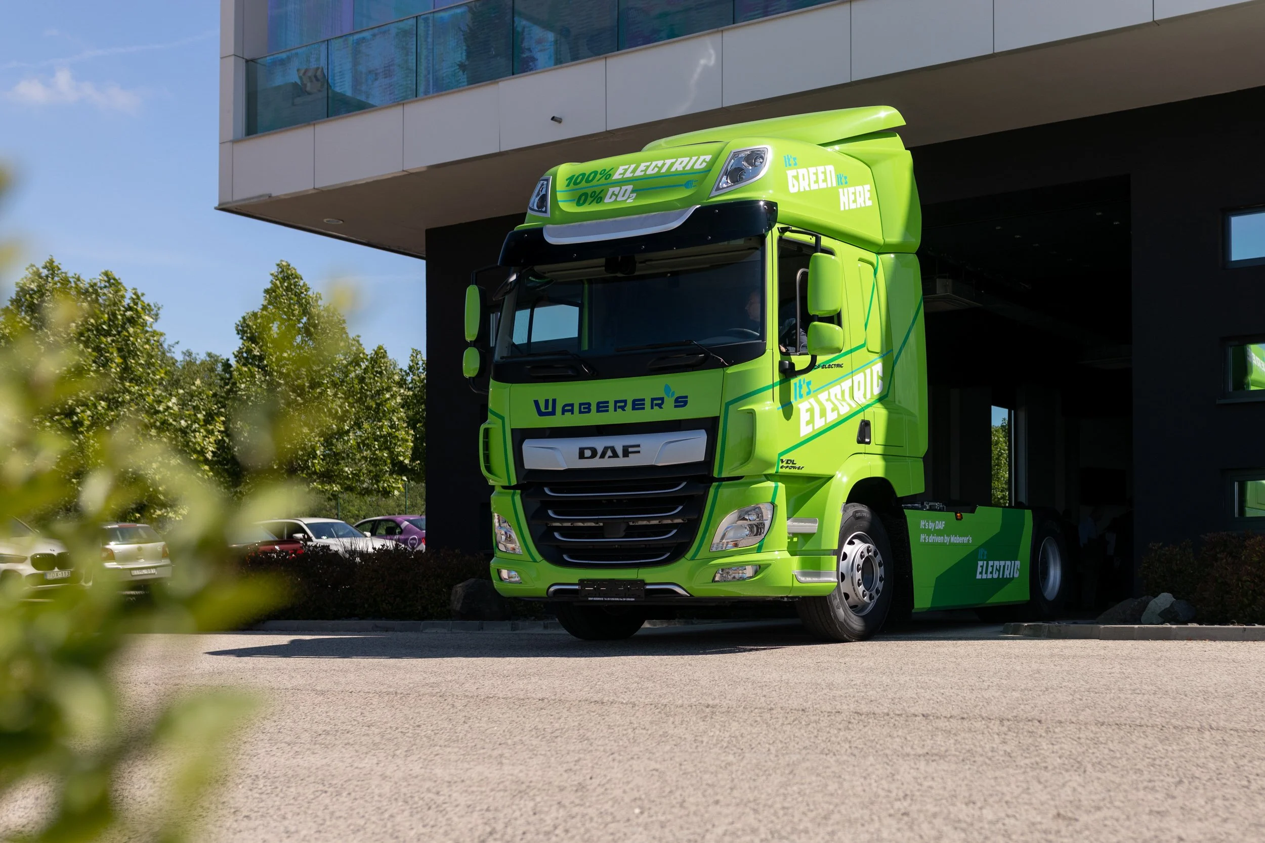 Bright green electric truck parked outside a modern building with glass windows.
