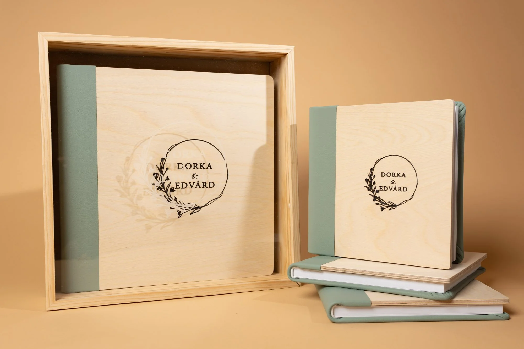 A set of light-colored wooden books with green accents, arranged in a wooden box and stacked on top of each other, with inscriptions reading 'Dorka & Edvard' inside a circular decoration on the covers.