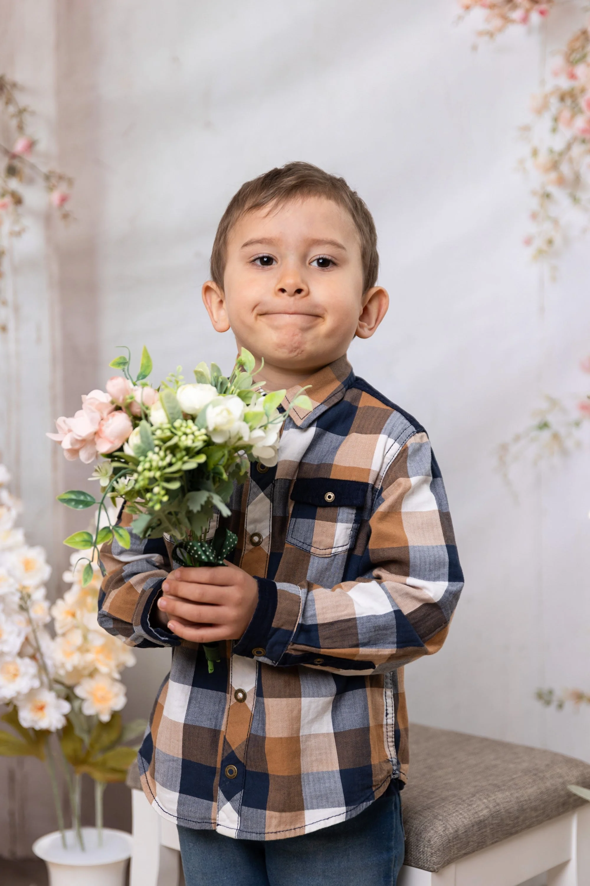 Young boy in a plaid shirt holding a bouquet of flowers in a room decorated with floral arrangements
