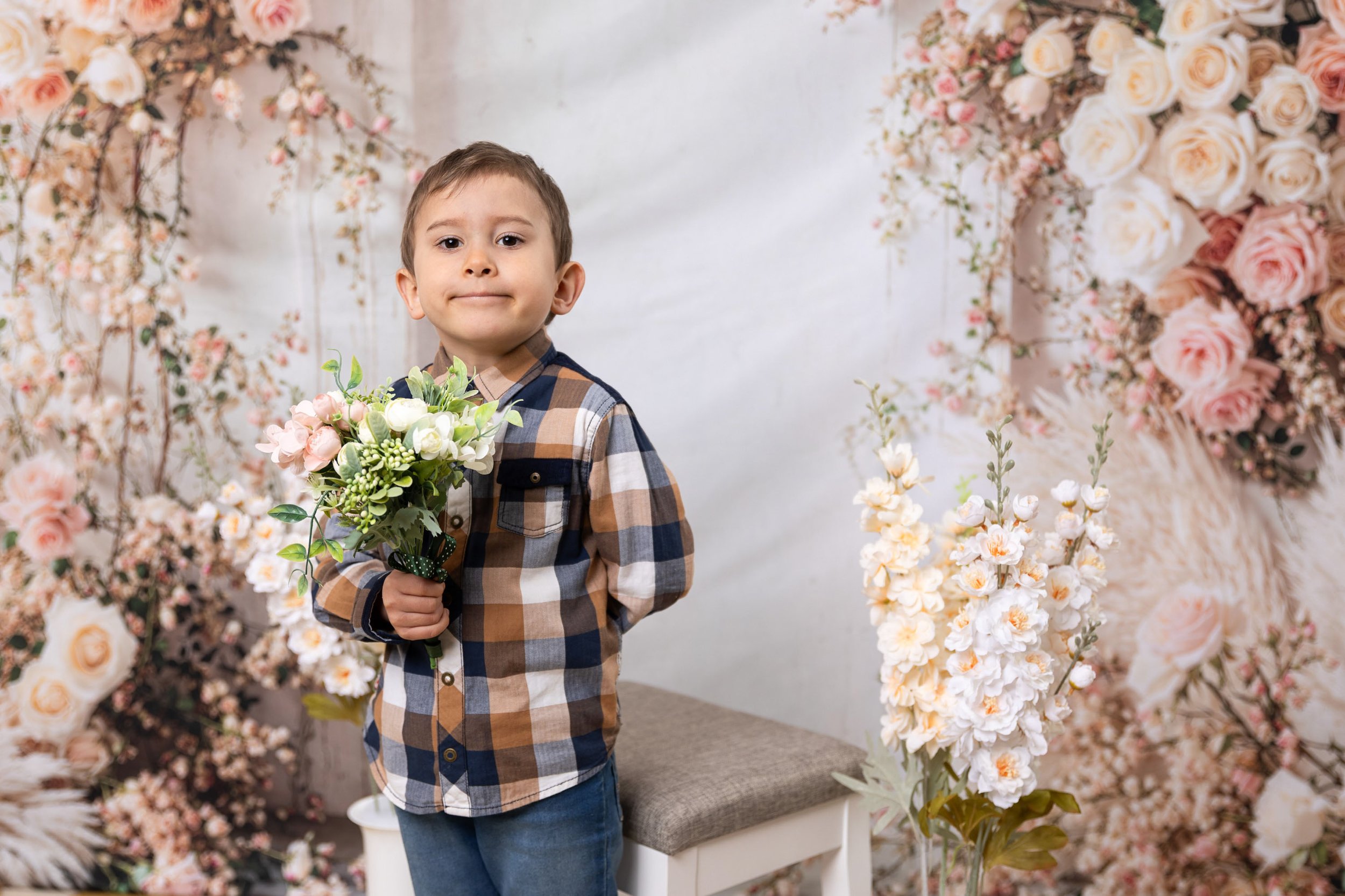 A young boy holding a bouquet of flowers in front of a floral backdrop.