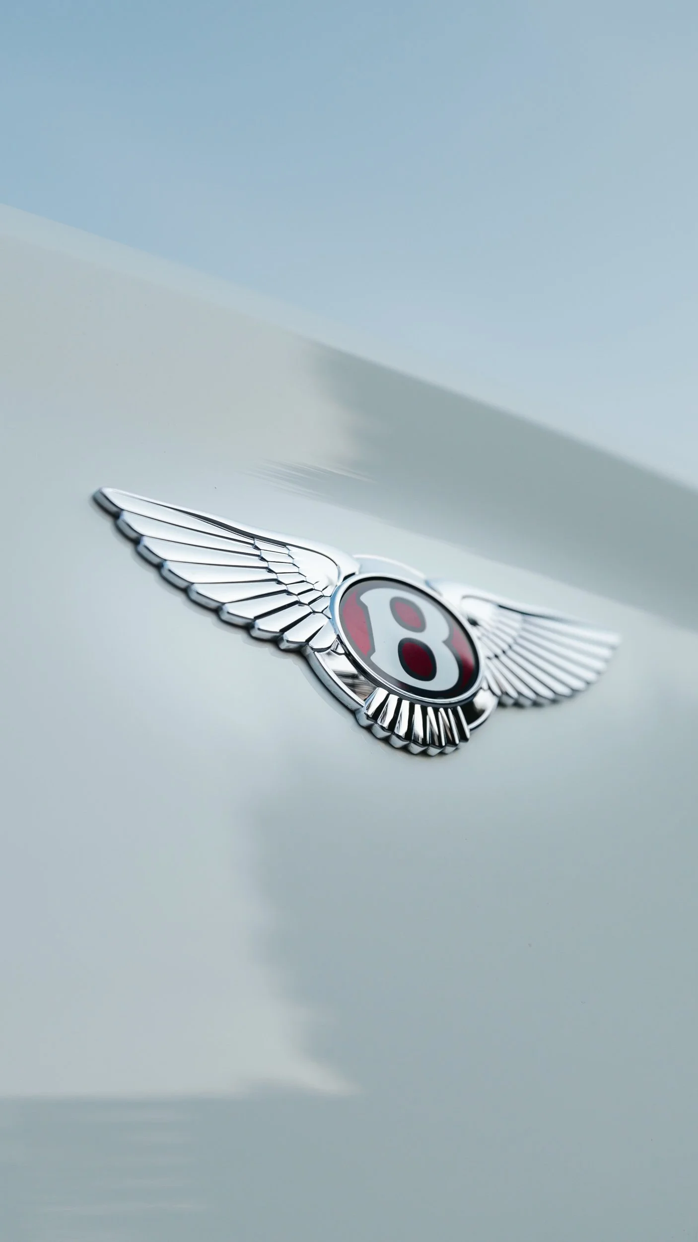 Close-up of a silver Bentley emblem with wings on a light-colored car surface.