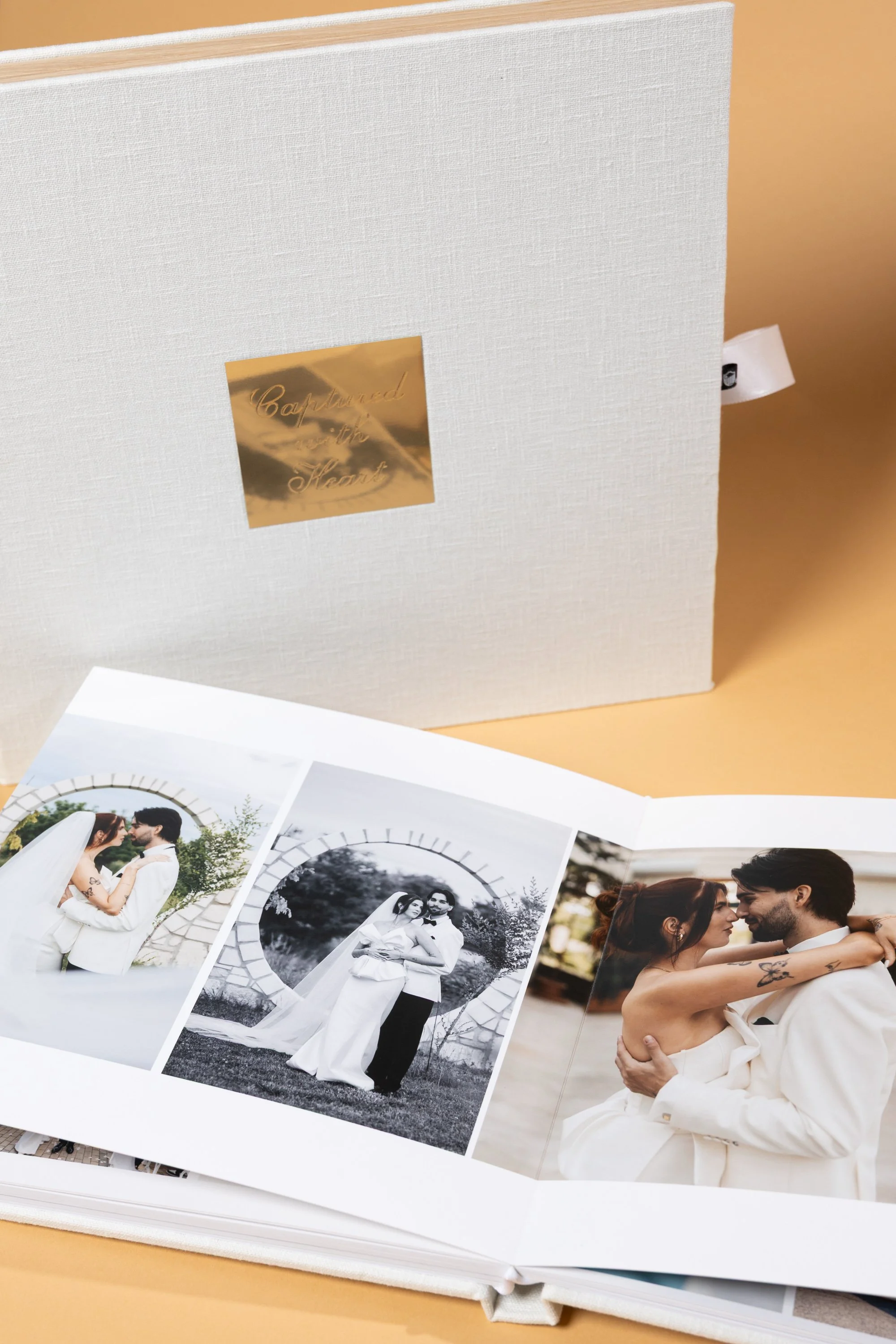 Open photo album with wedding photos of a couple, some in color and some in black and white, in front of a beige background.