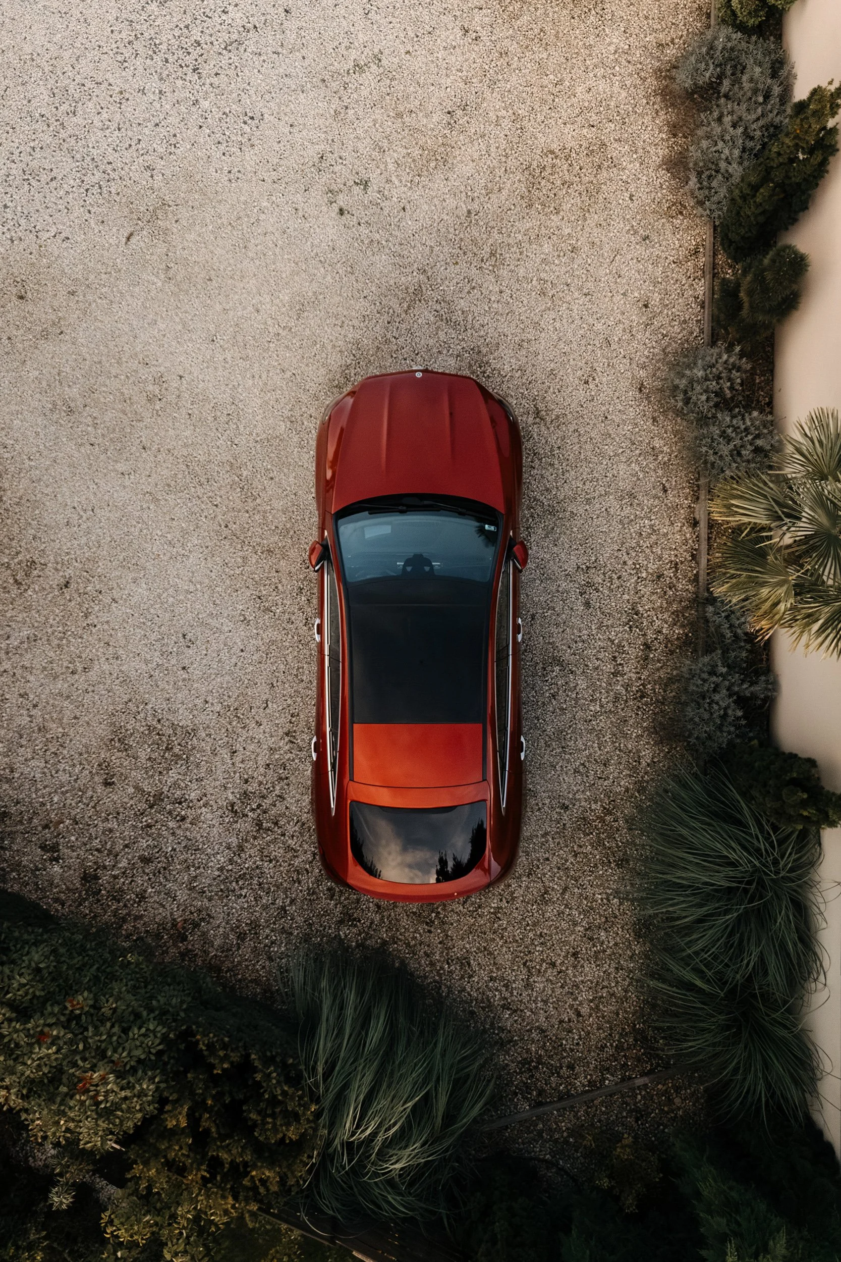 An aerial view of a red car parked on a gravel driveway next to desert-like plants.