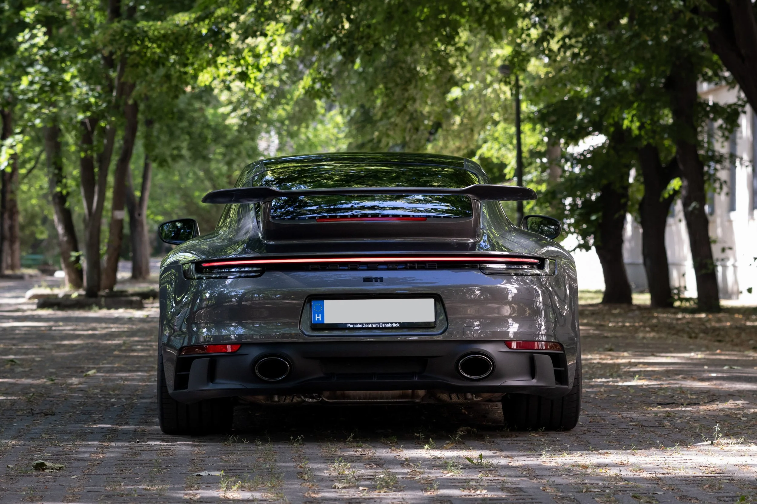 Rear view of a black Porsche sports car parked on a tree-lined street.