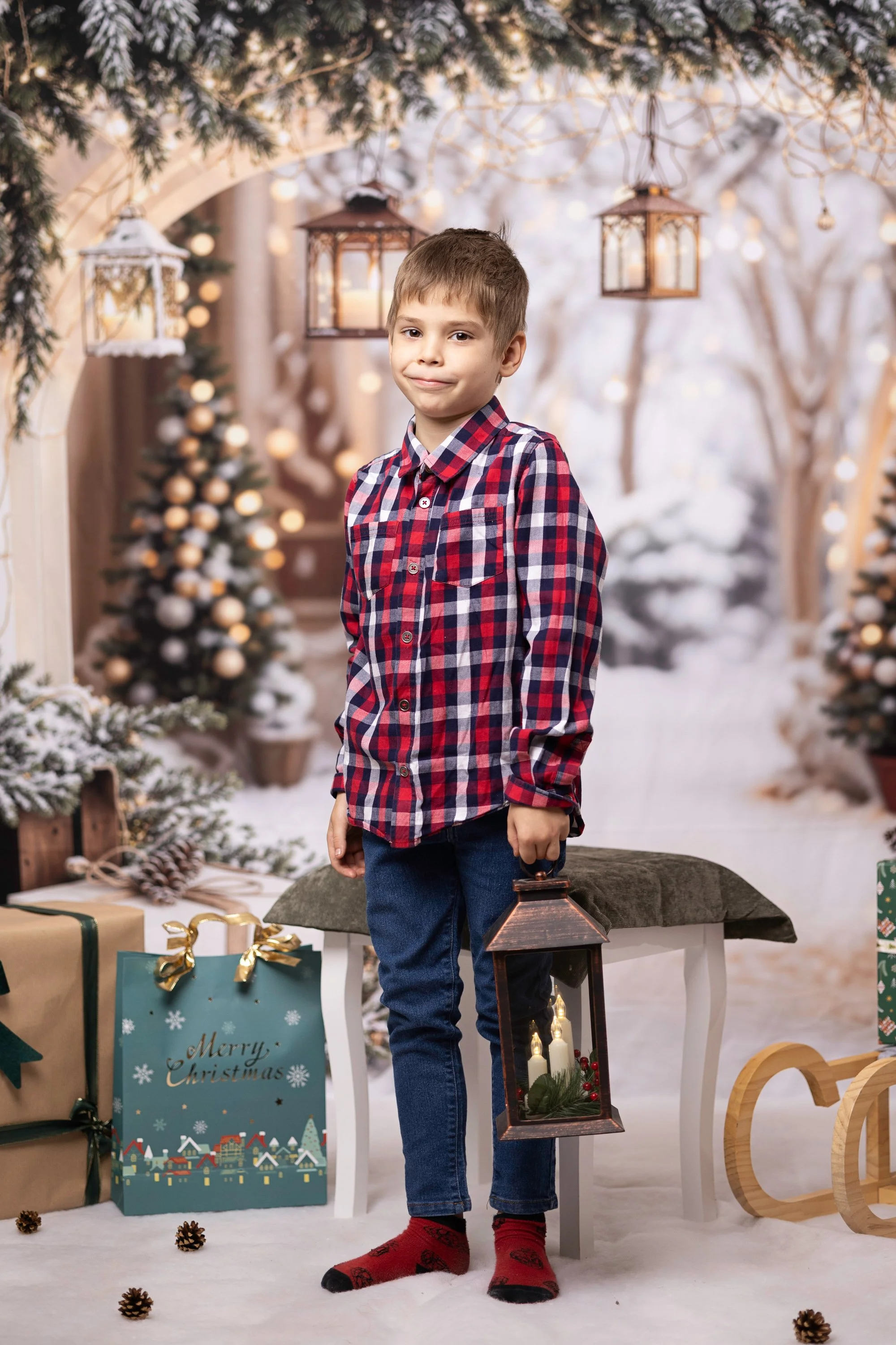 A young boy dressed in a red and blue plaid shirt and jeans, holding a lantern, standing in a festive Christmas setting with gifts, decorated trees, and holiday ornaments.