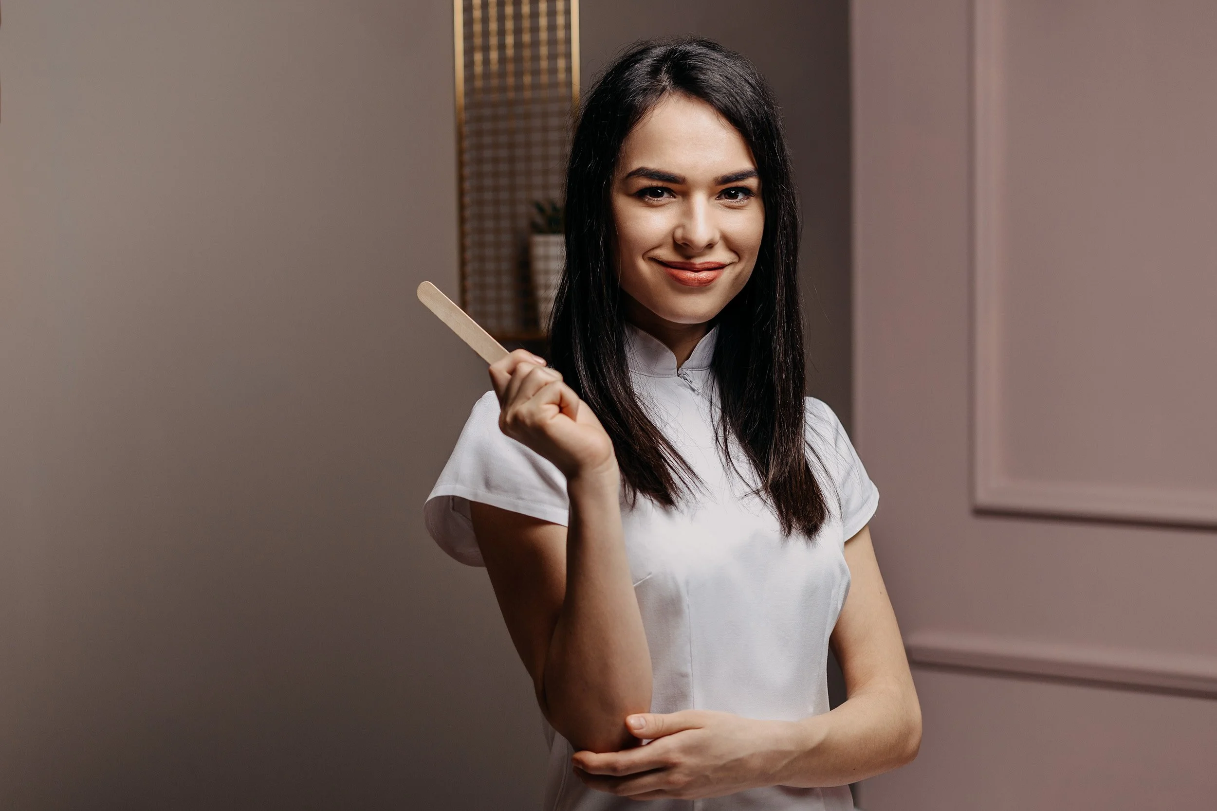 A woman with long dark hair smiling and holding a wooden popsicle stick.