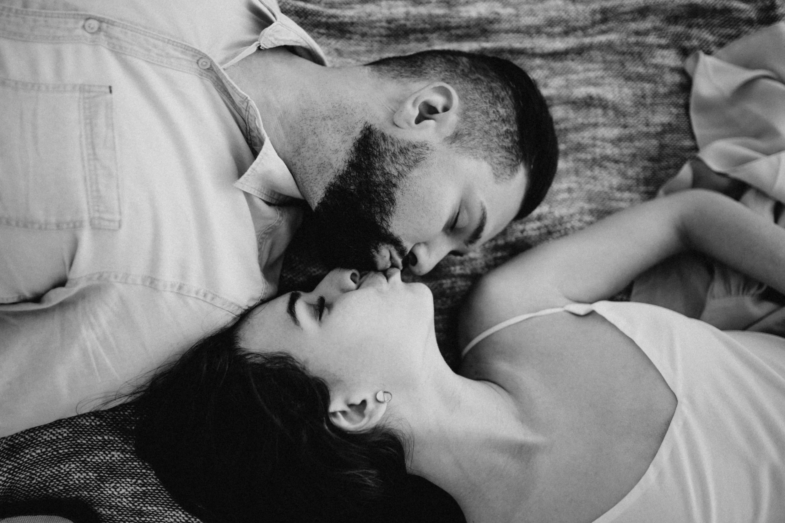 A black and white photo of a man and woman lying close together, touching their foreheads, with their eyes closed, sharing an intimate moment.