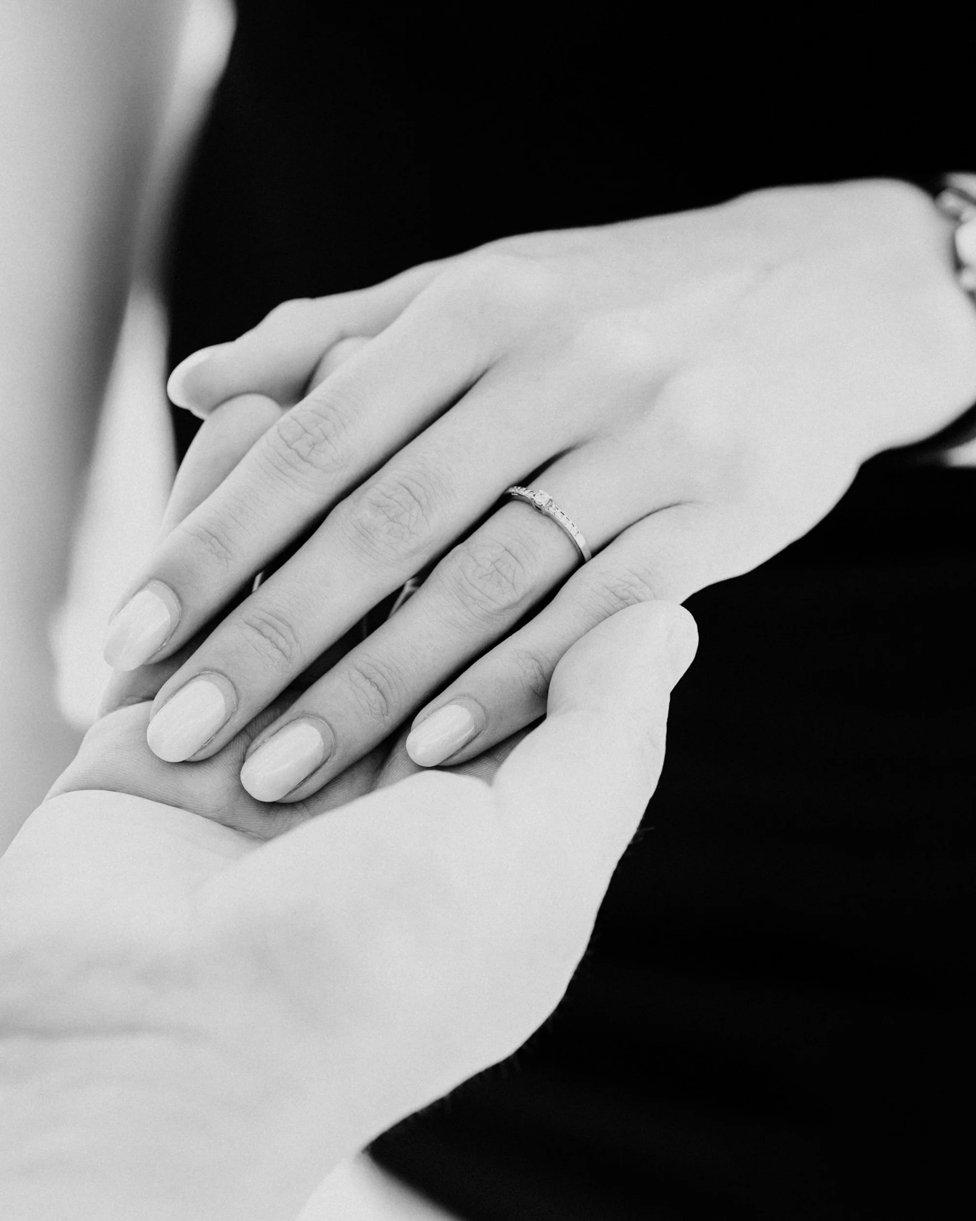 Close-up of a hand with a ring touching another hand, in black and white photo.