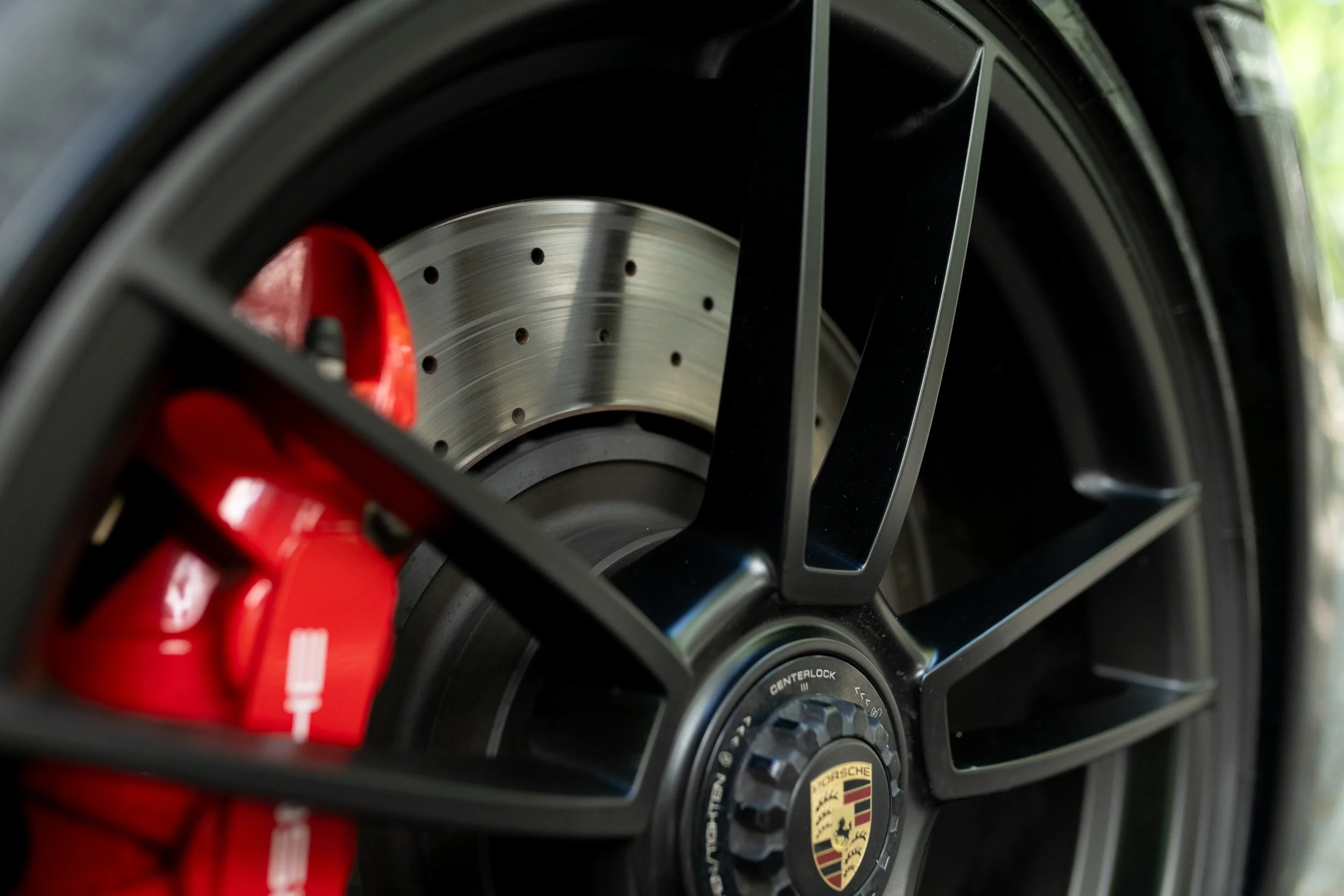 Close-up of a Porsche sports car wheel with a metallic brake disc and red brake caliper.
