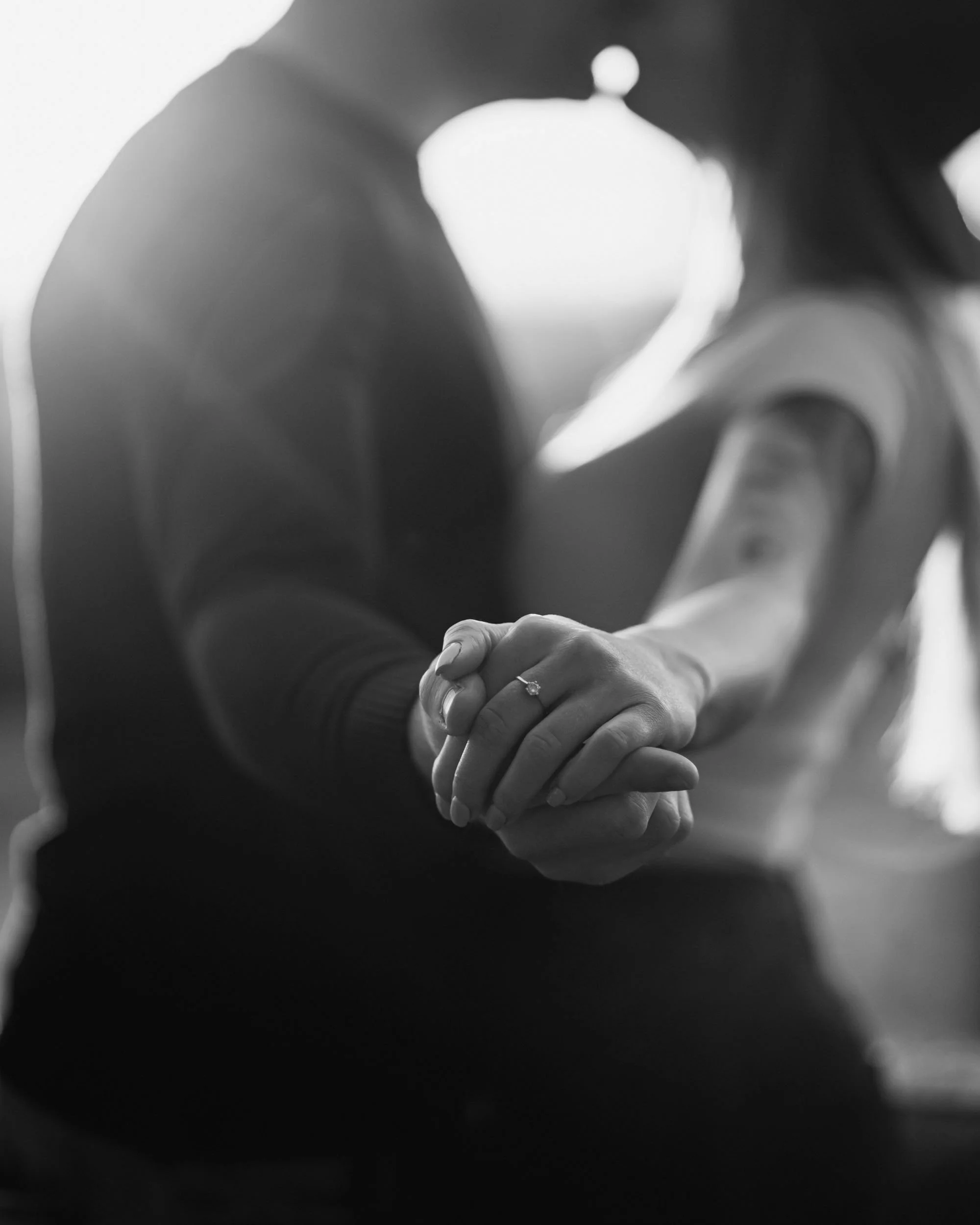 Black and white photo of two people holding hands, with one person wearing a ring on their ring finger.