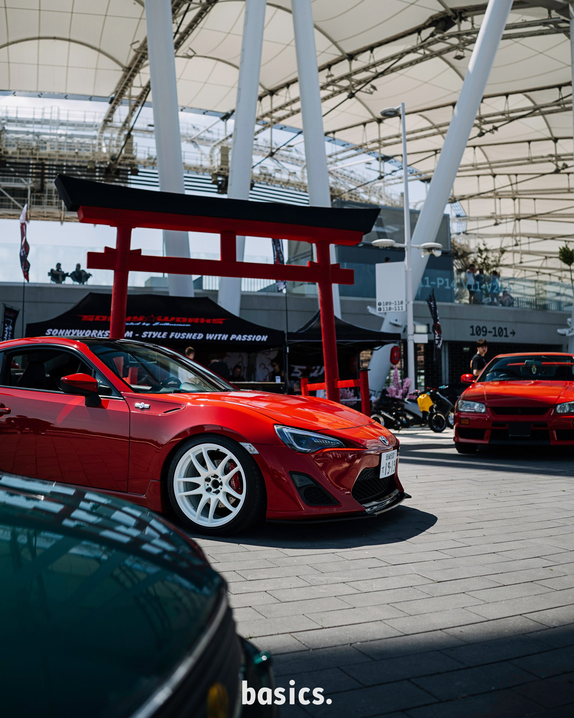 Piros Toyota gt86 japán kapuval mögötte a Nemzeti atlétikai központ stadionnál fotózva a Basics 2026 rendezvényen