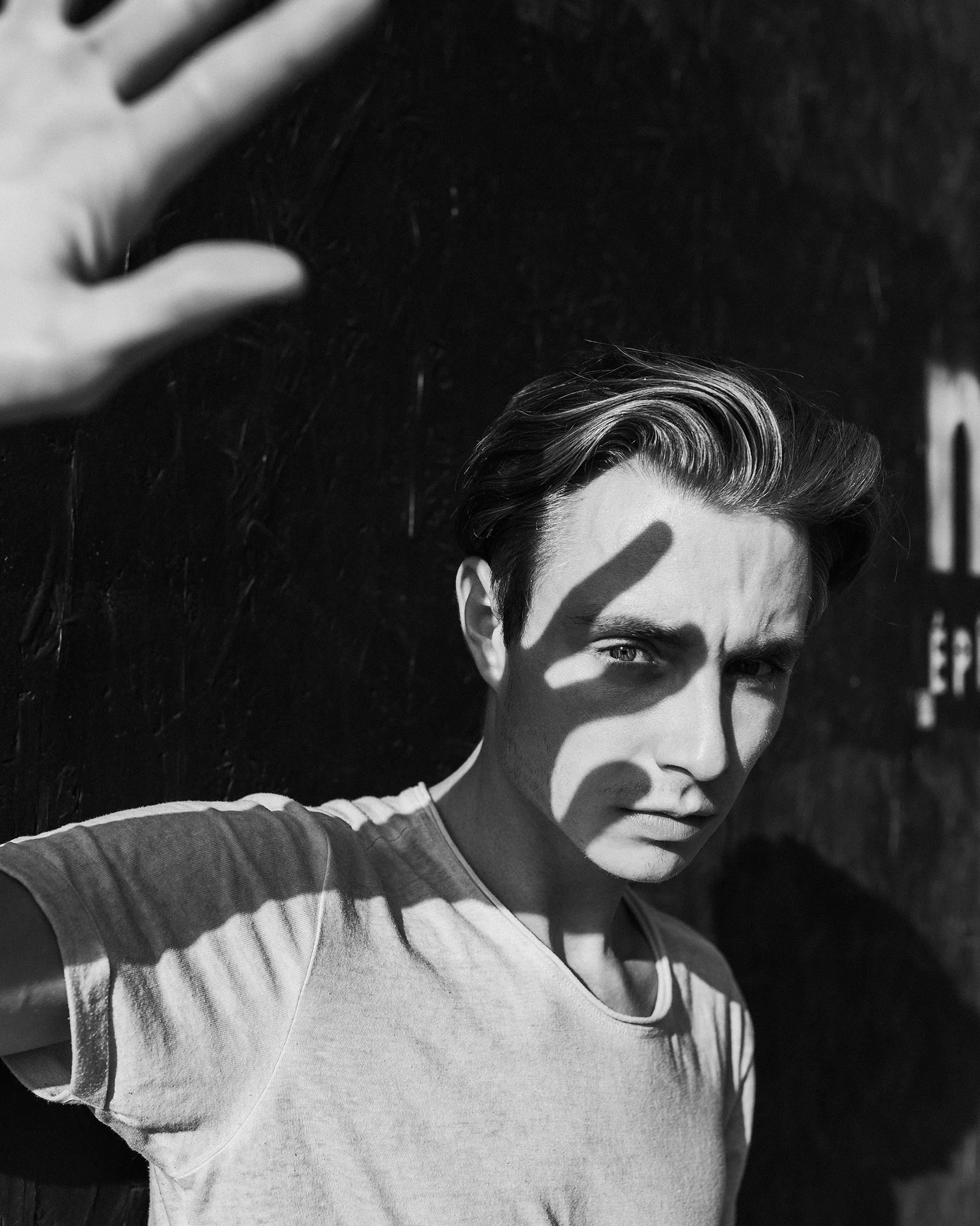A black and white image of a woman taking a selfie, with sunlight casting shadows on her face and hair.