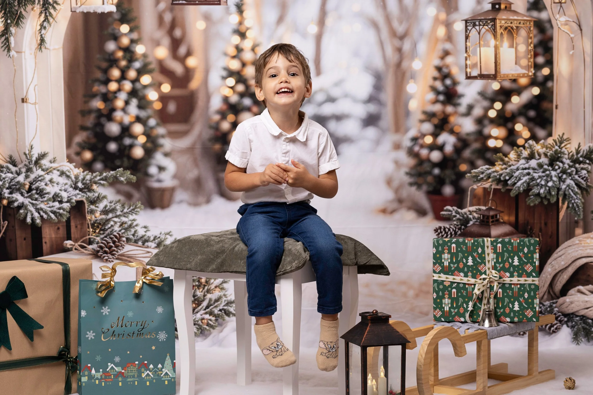 A young boy sitting on a stool surrounded by Christmas decorations, including Christmas trees, wrapped gifts, and holiday ornaments, in a festive setting with snow and warm lighting.