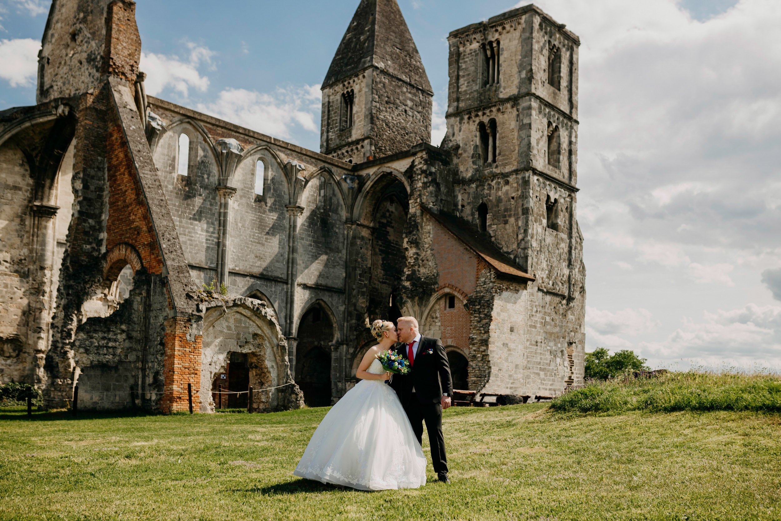 A newlywed couple sharing a kiss in front of an ancient stone church on their wedding day.