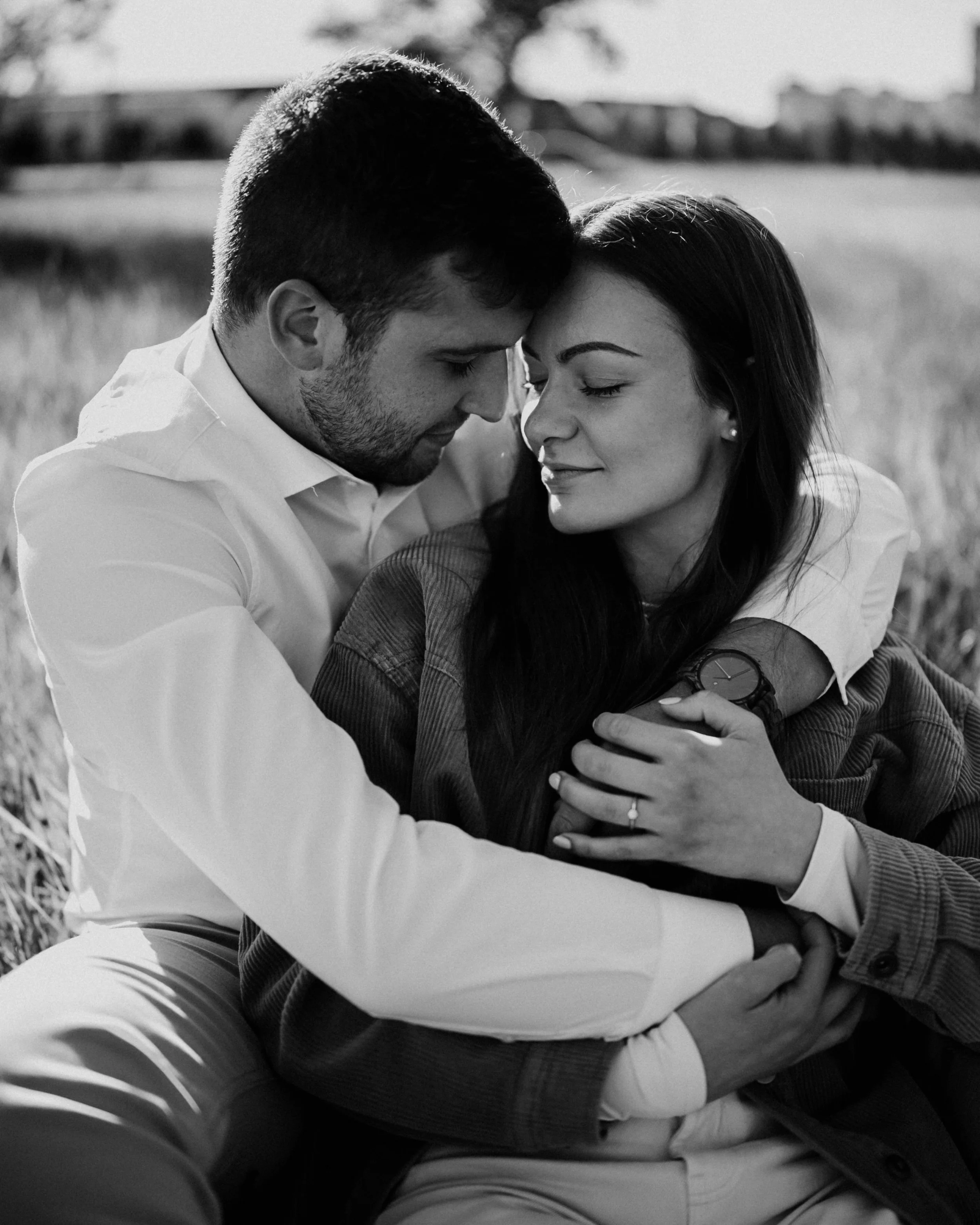 A black and white photograph of a young man and woman embracing outdoors, with their foreheads touching and eyes closed, showing affection and intimacy.