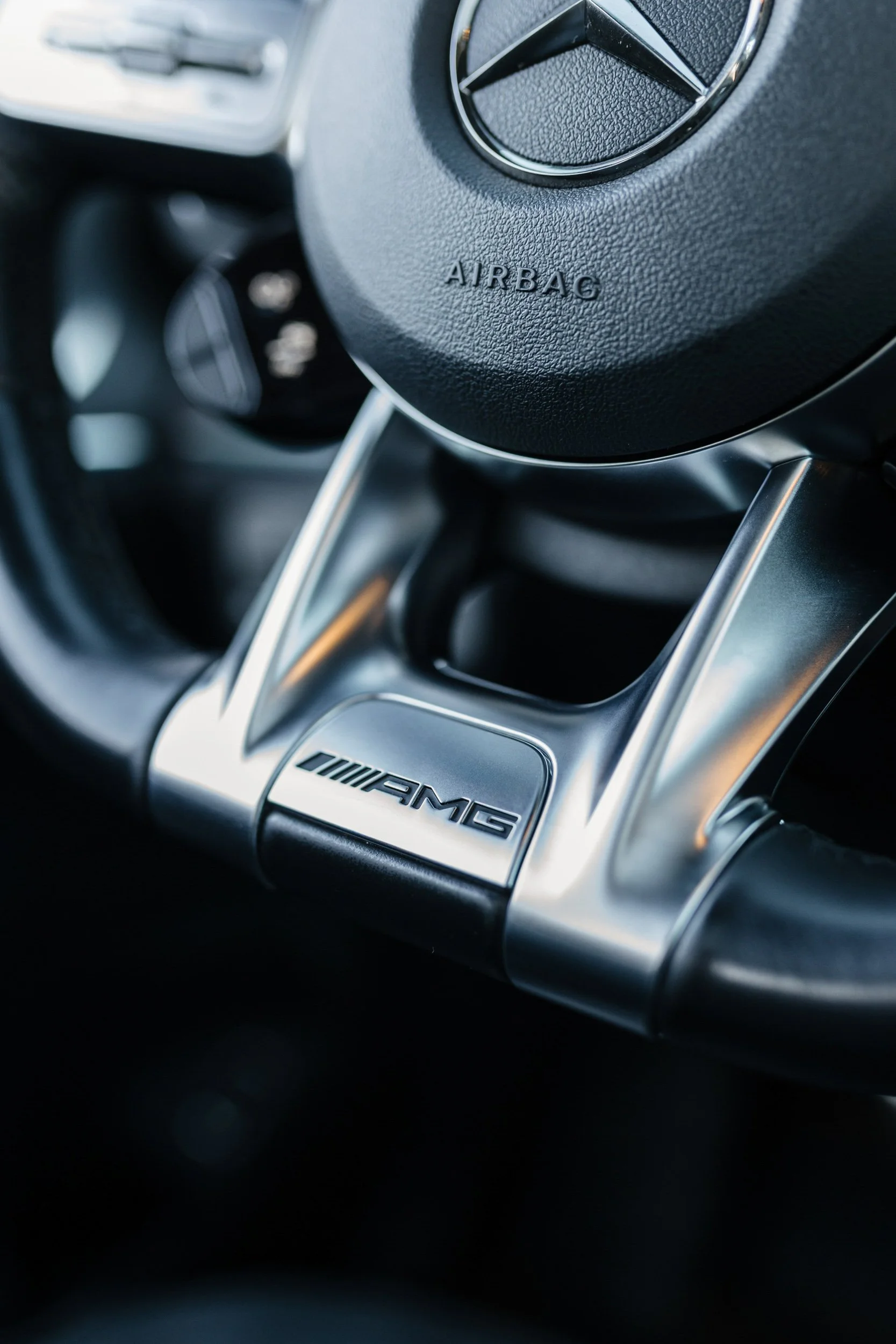 Close-up of a Mercedes-Benz steering wheel with the AMG logo, showing the Mercedes logo and the word 'AIRBAG' on the textured black surface.
