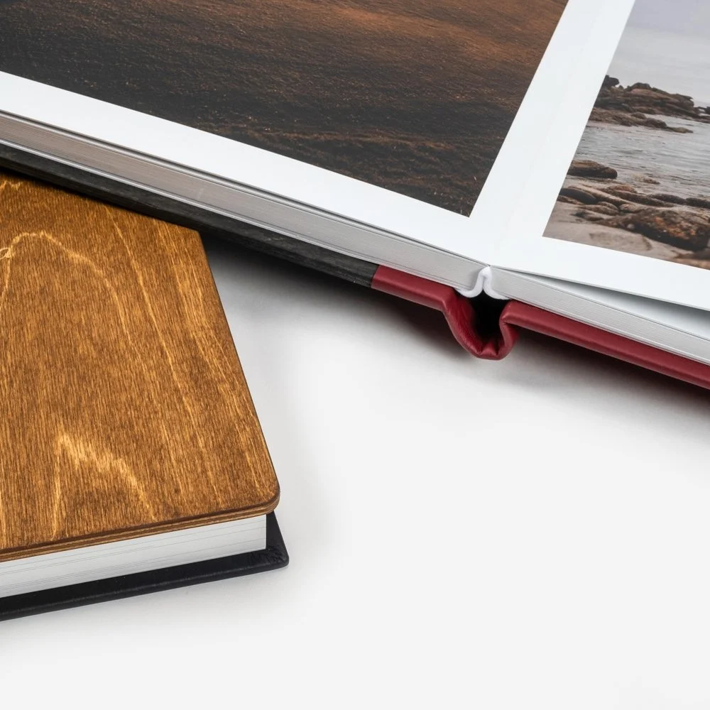 Close-up photo of two books, one with a wooden cover and the other open, displaying landscape photographs, on a white surface.