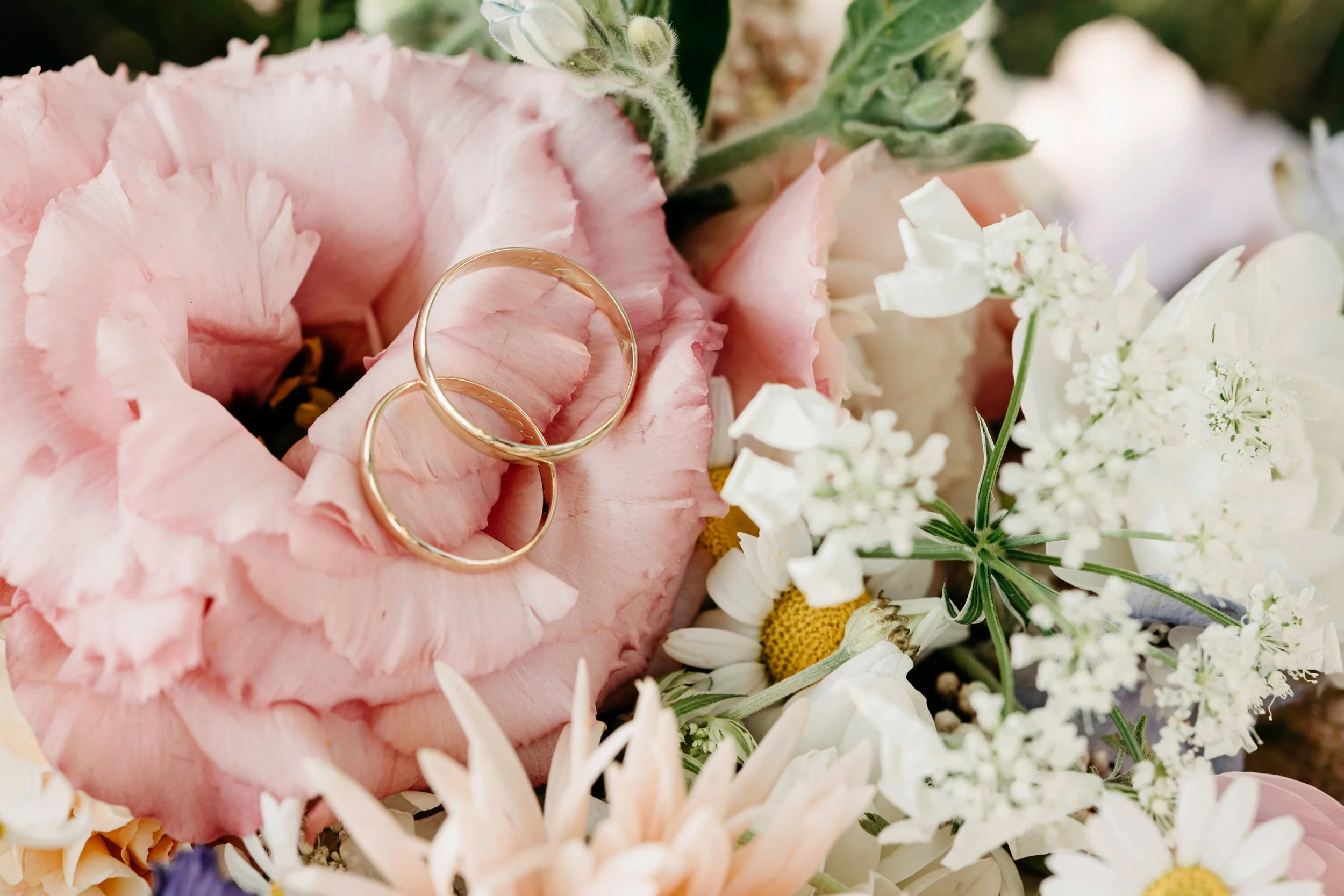 Close-up of a bouquet of pink and white flowers with two gold wedding rings placed on pink flowers.