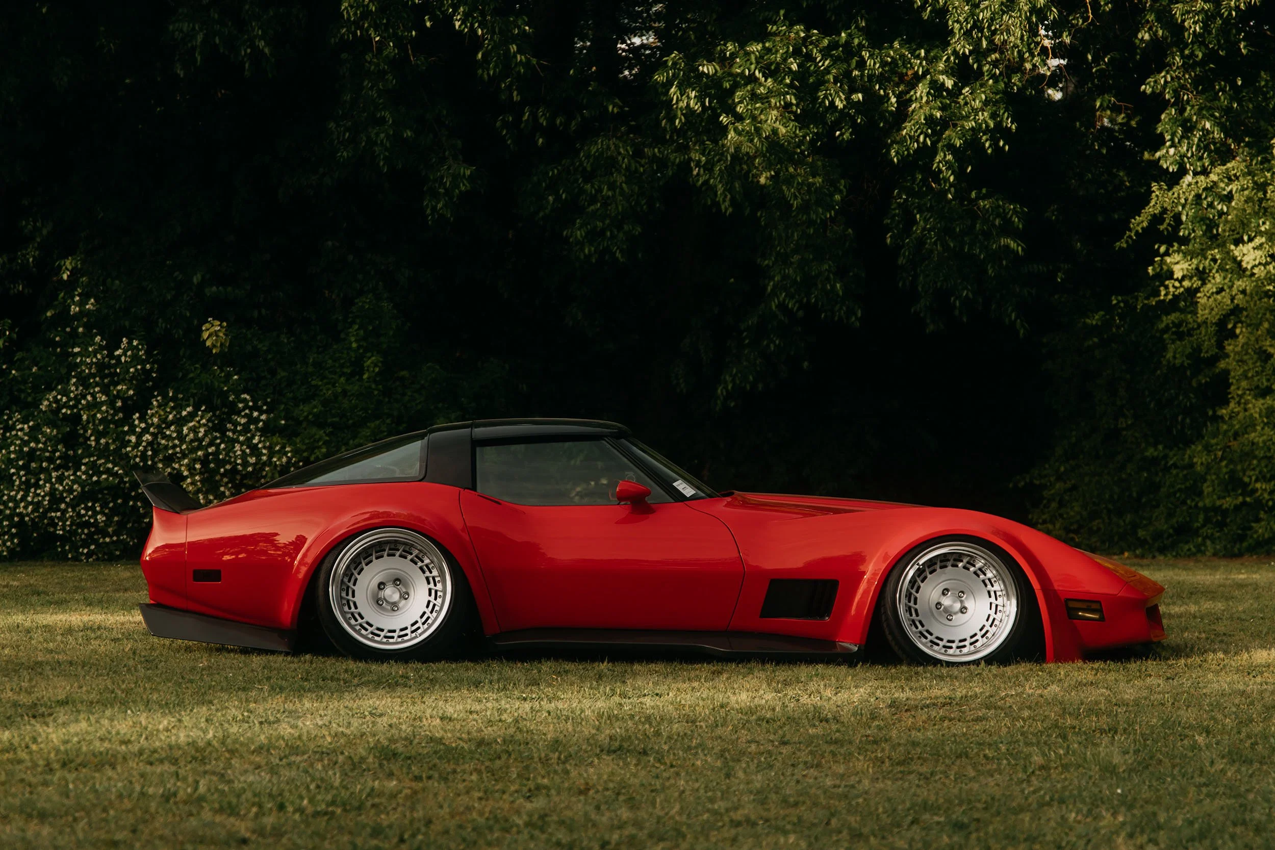 Red sports car parked on grass with trees in the background.