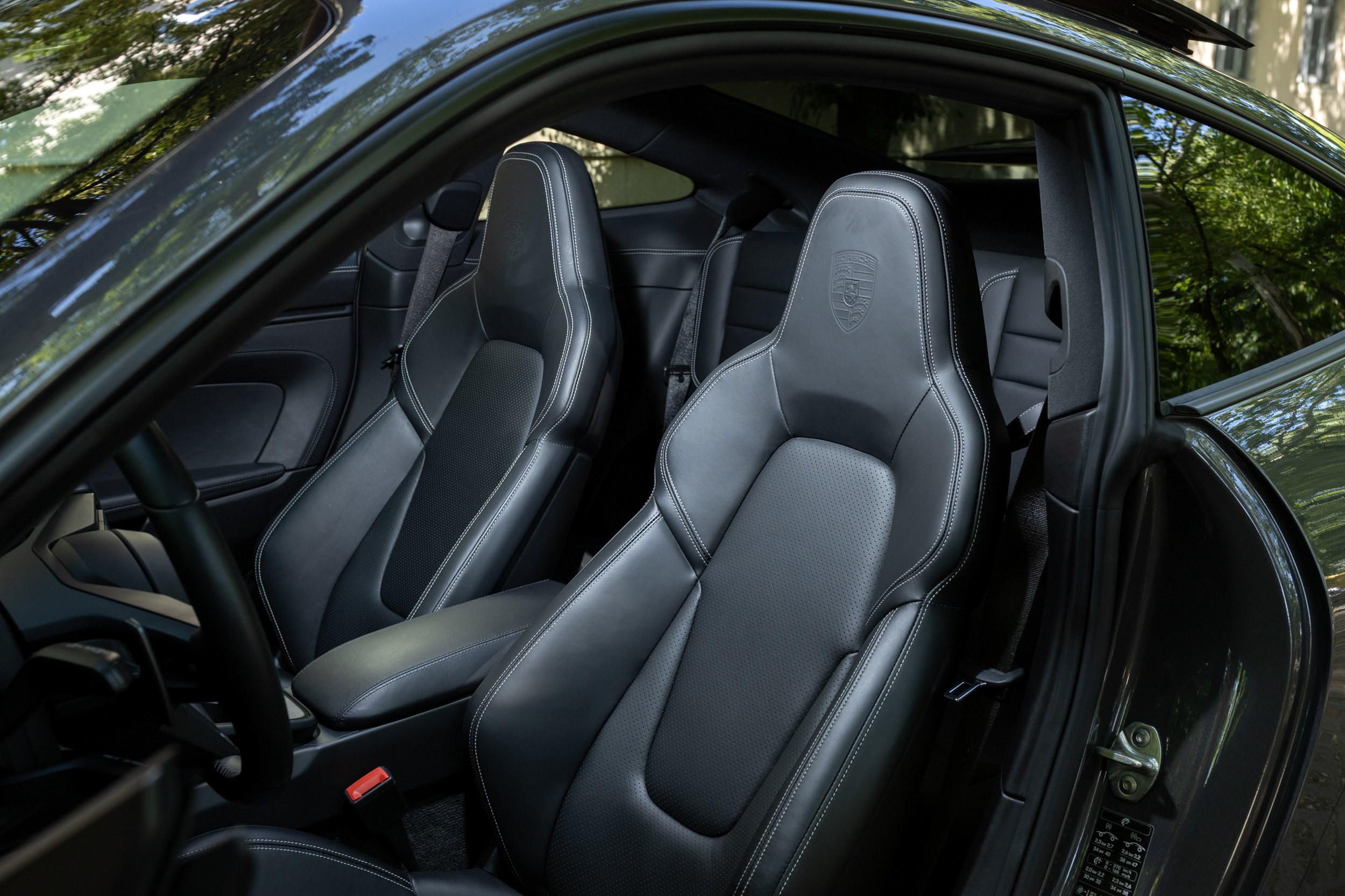 Interior of a car showing black leather seats with Porsche logo embossing, detailed stitching, and a view of the headrests and side windows.