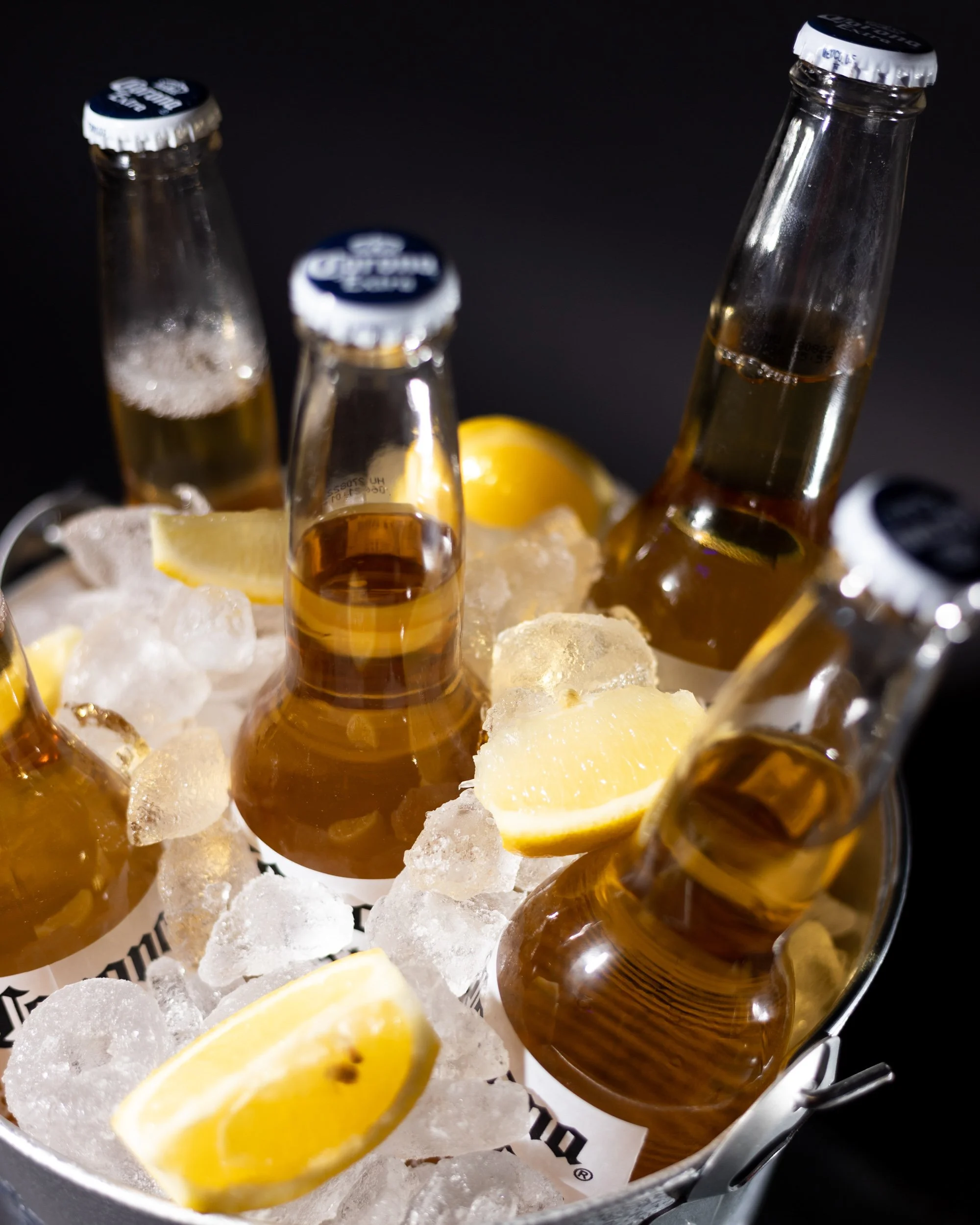Close-up of bottles of beer and lemon wedges on ice in a metal container.