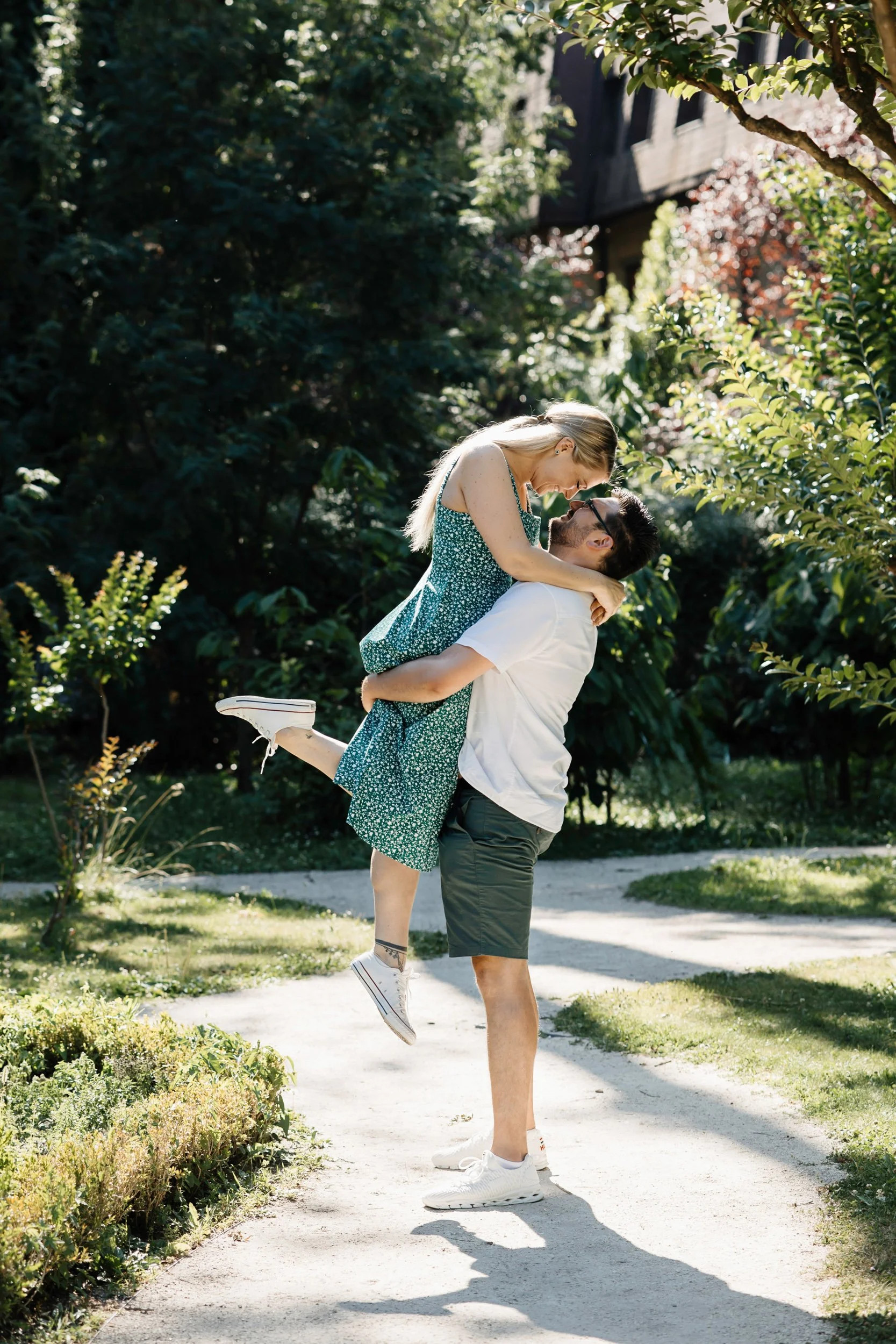 A man lifting a woman in a garden with greenery and trees, both smiling and enjoying each other's company.