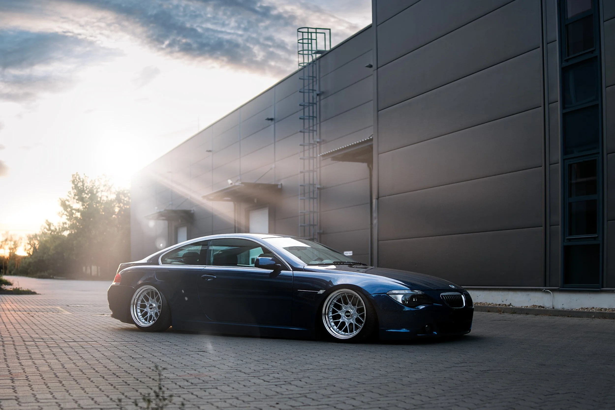 A black sports car parked outside a modern building during sunset.