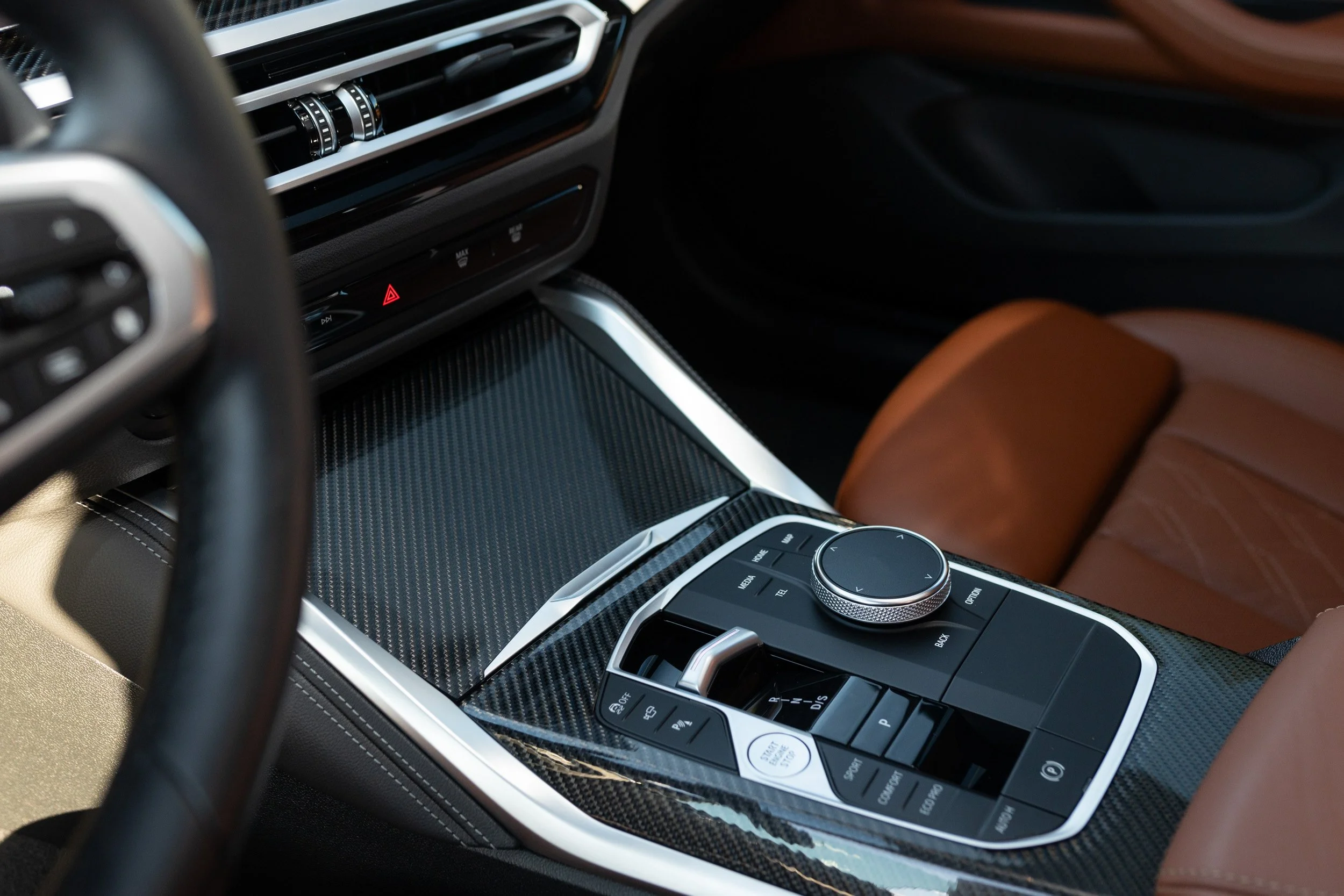 Interior view of a luxury car, showing the center console with controls, gear shifter, and brown leather seat.