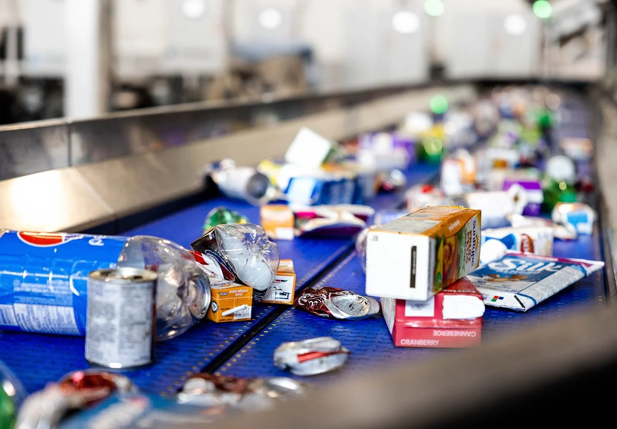 Litter of crushed cans and food packaging on a recycling conveyor belt.