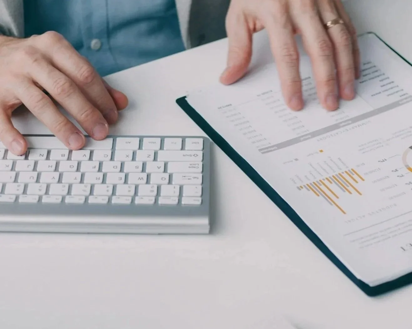 Person working at a desk with a computer keyboard and financial documents displaying charts and data.