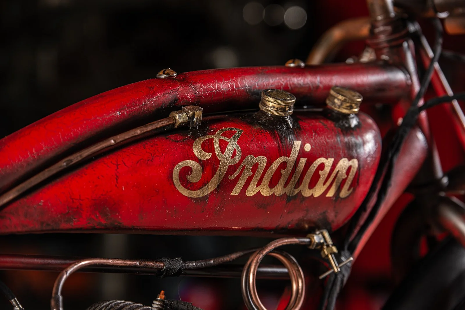 Board track racer red Indian motorcycle fuel tank with rust, wear, and the Indian logo in gold lettering.
