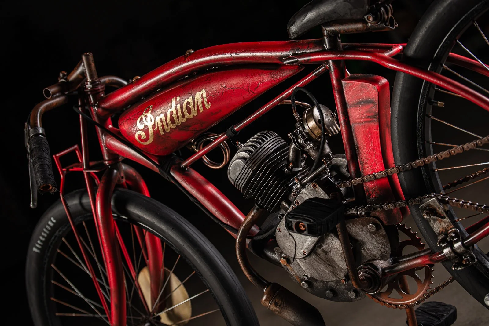 Board track racer Indian motorcycle with a red frame, black tires, and a visible engine, set against a black background.