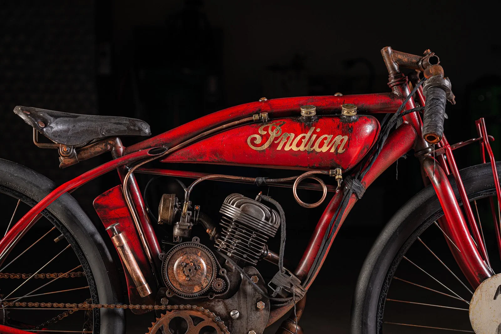 A vintage red Indian motorcycle with rust, showing the engine, seat, and frame.